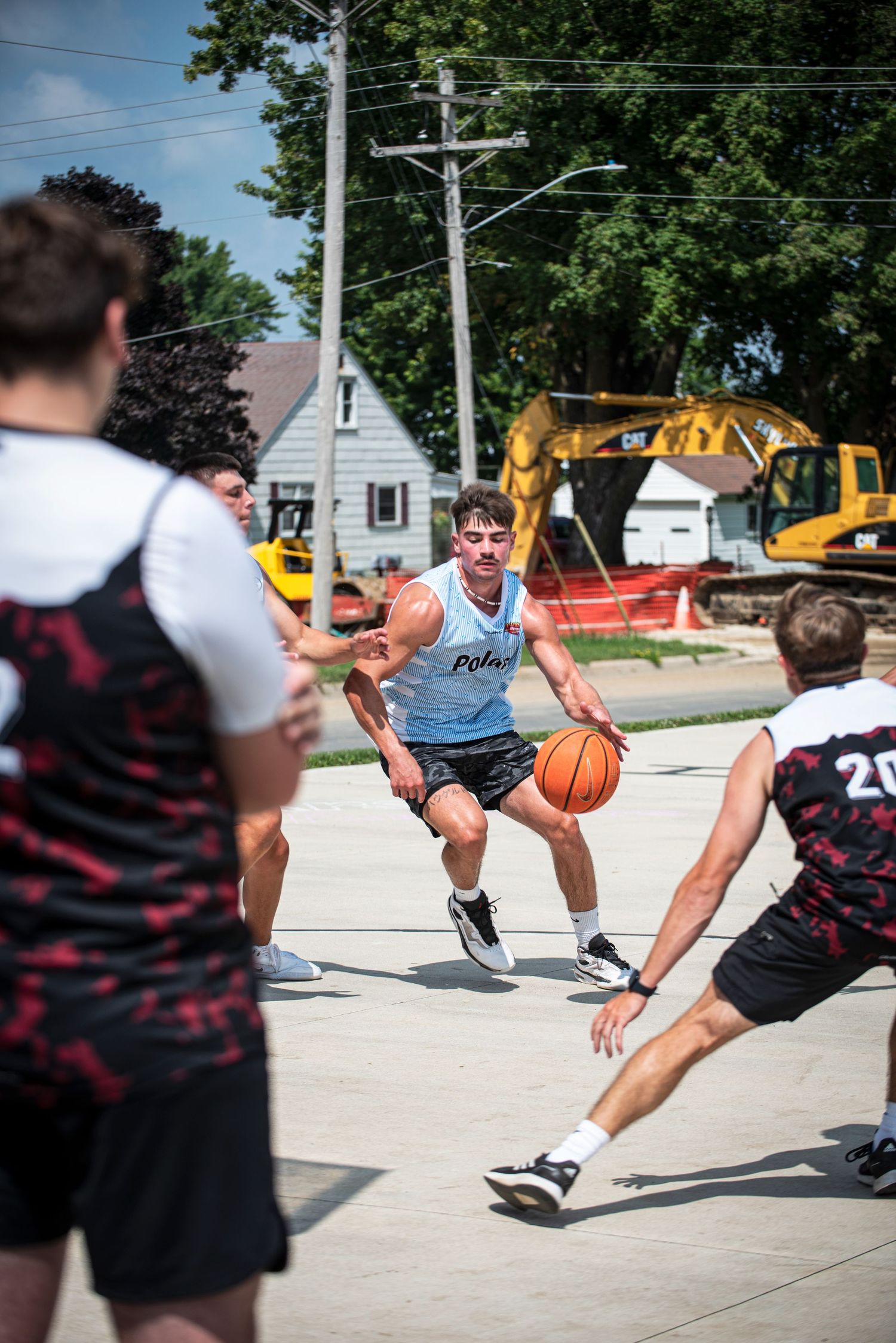 Basketball player in blue jersey drives through defenders on outdoor concrete court.