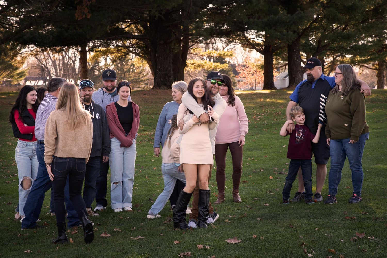 A large multigenerational family laughs and embraces together on a grass lawn during an outdoor photo session.