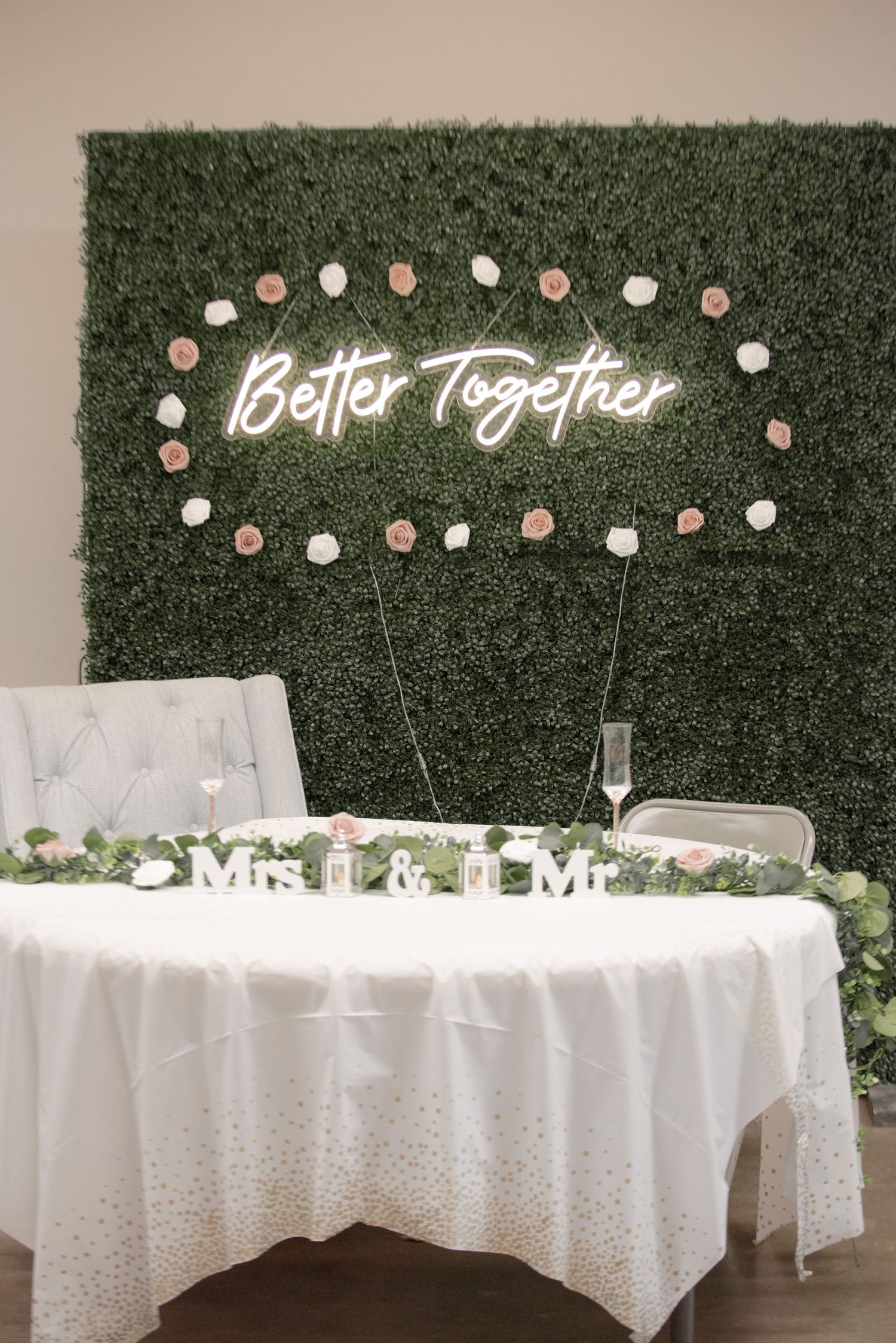 Elegant wedding sweetheart table with a green floral wall and Better Together neon sign.