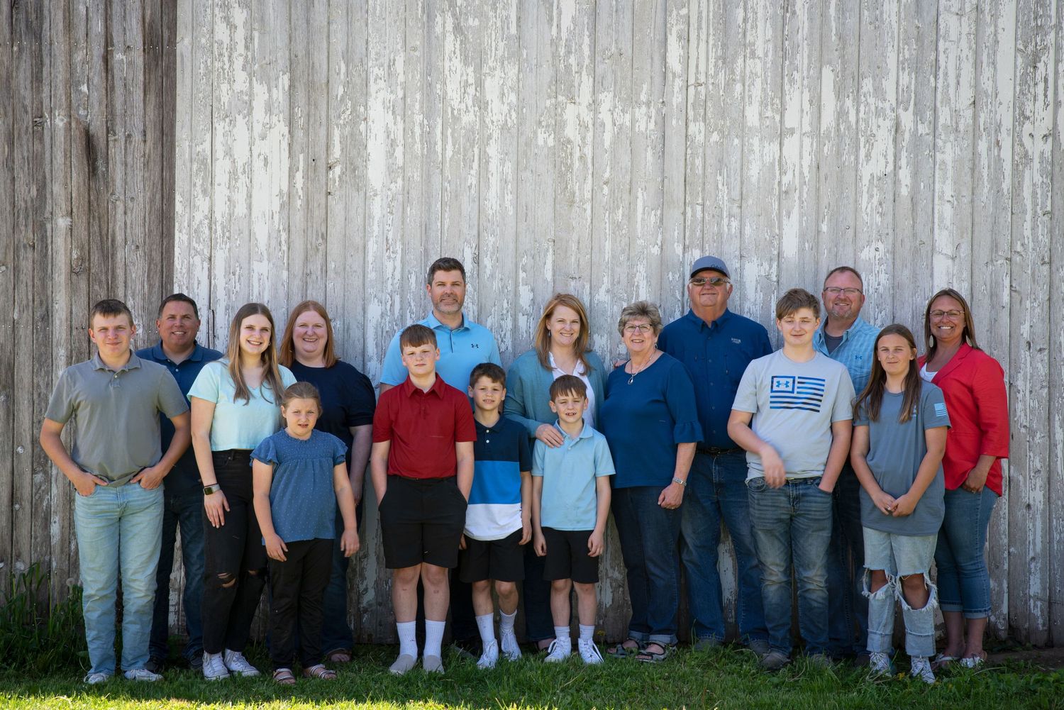 Large extended family portrait standing together in front of a weathered gray barn wall.