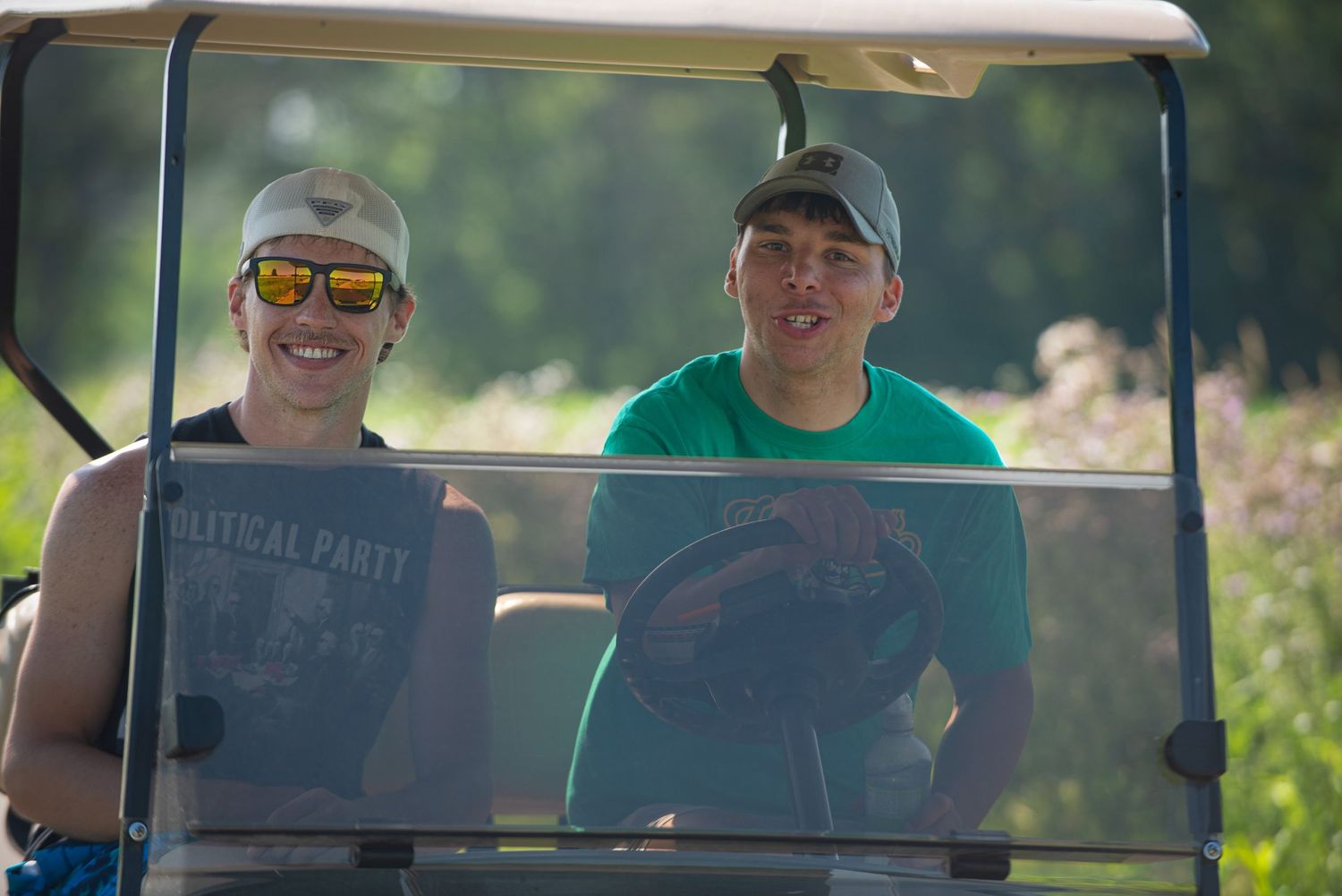 Two young men smiling in golf cart on sunny day outdoors at Harmony MN 4th of July Celebration..