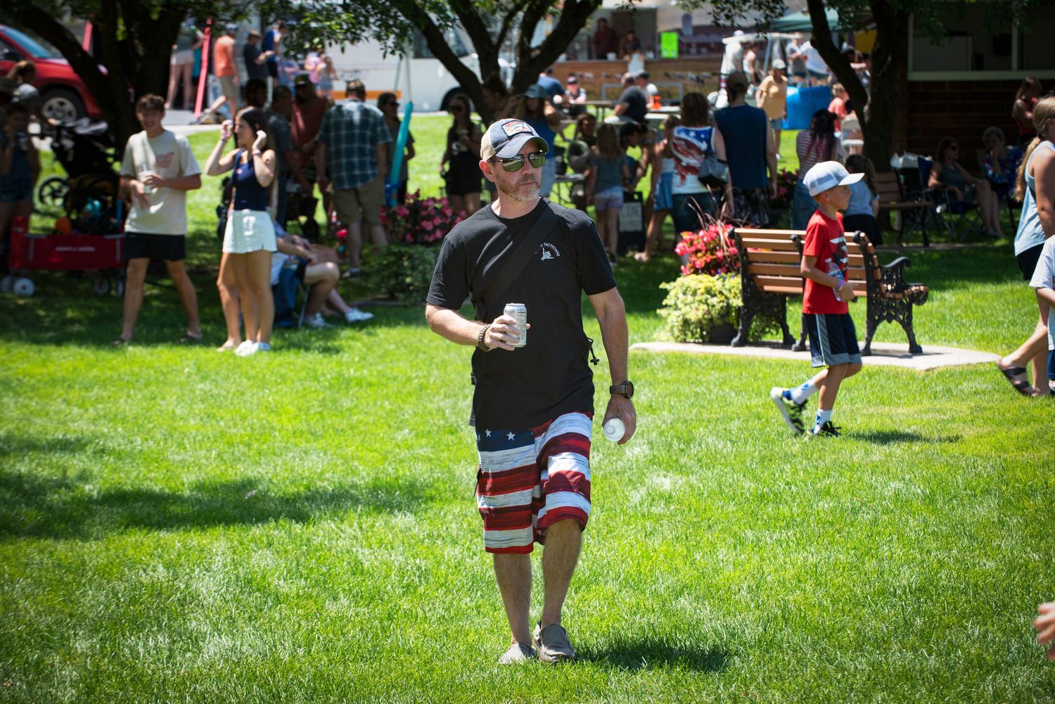 A man in American flag shorts enjoys a drink on a sunny green lawn at a summer celebration. At Harmony MN 4th of July Celebration.