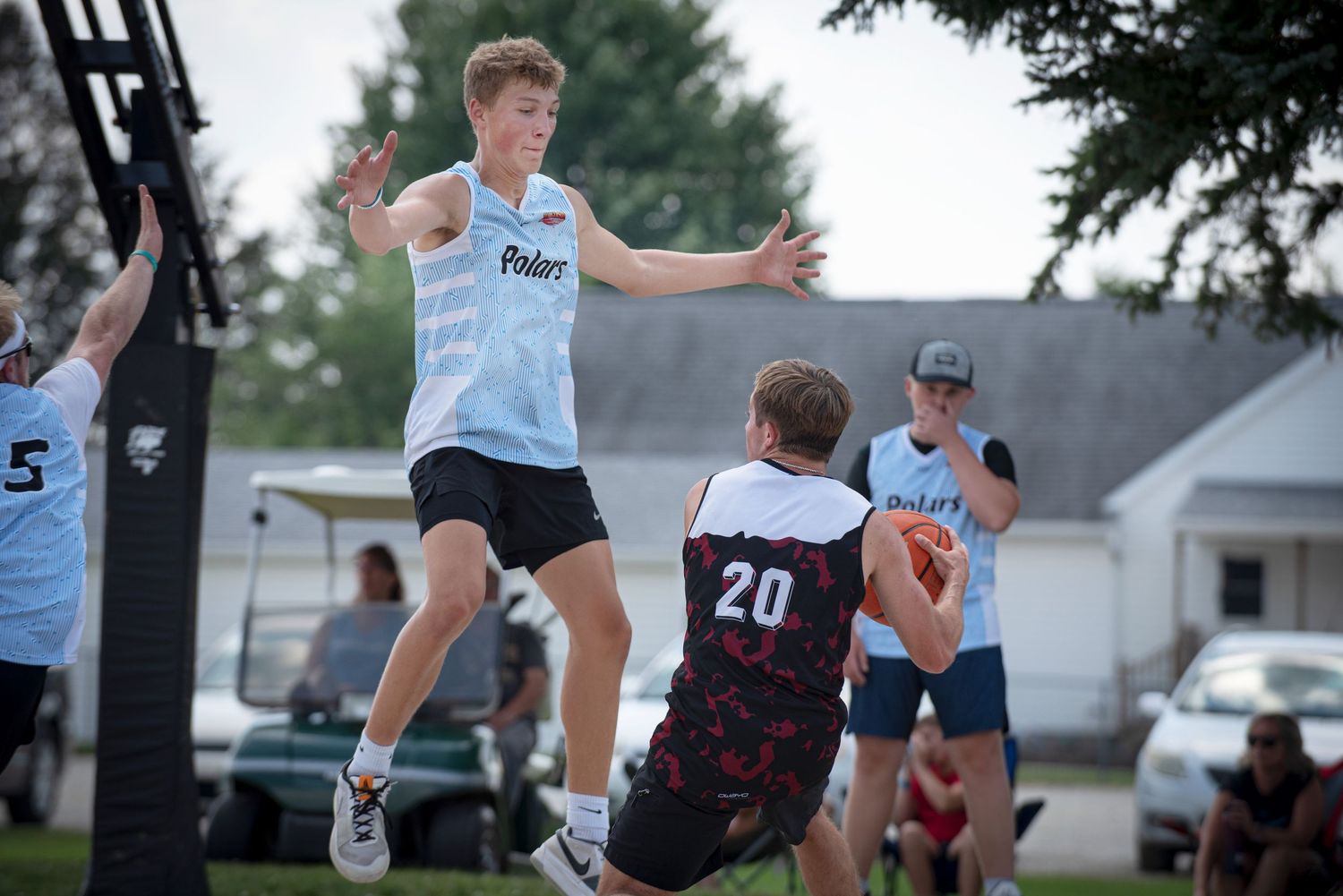 Tall player in blue jersey leaps to block pass attempt during outdoor Rucker League basketball game.