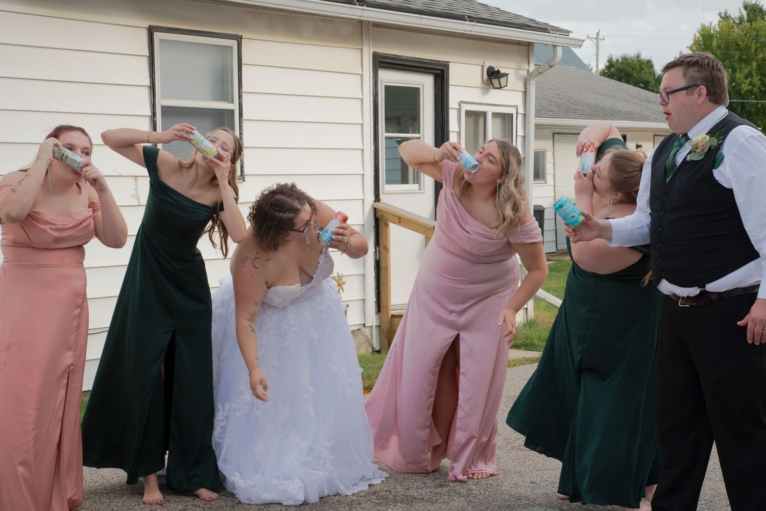Wedding party in green and pink dresses doing fun shots together outside a white building.