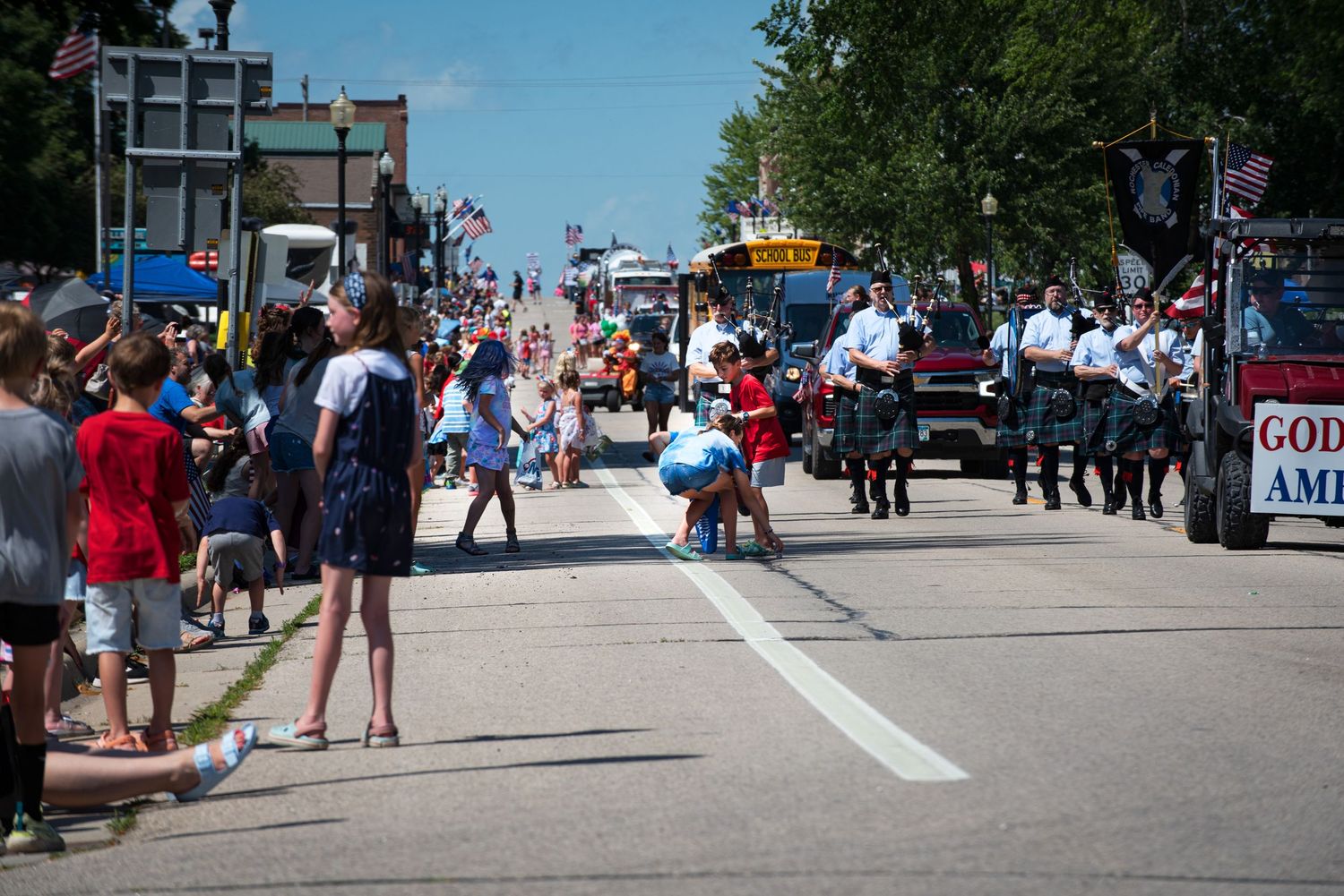 Spectators watch a patriotic small-town Fourth of July parade featuring bagpipers and a God Bless America float. At Harmony MN.