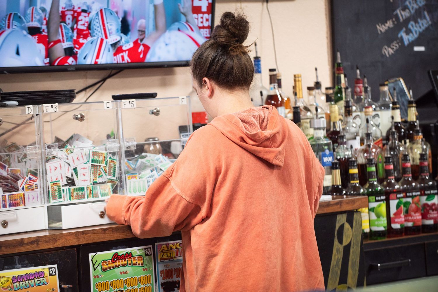 Young woman standing at a bar counter with colorful liquor bottles on shelves behind her at The Bite.