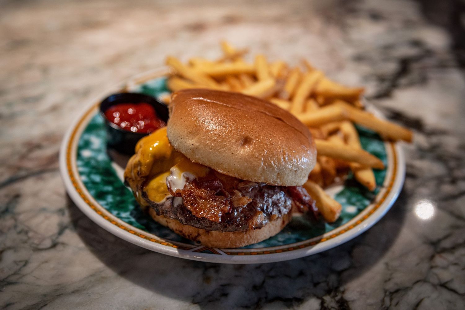 Gourmet cheeseburger with fries and dipping sauce served on a marble restaurant table.