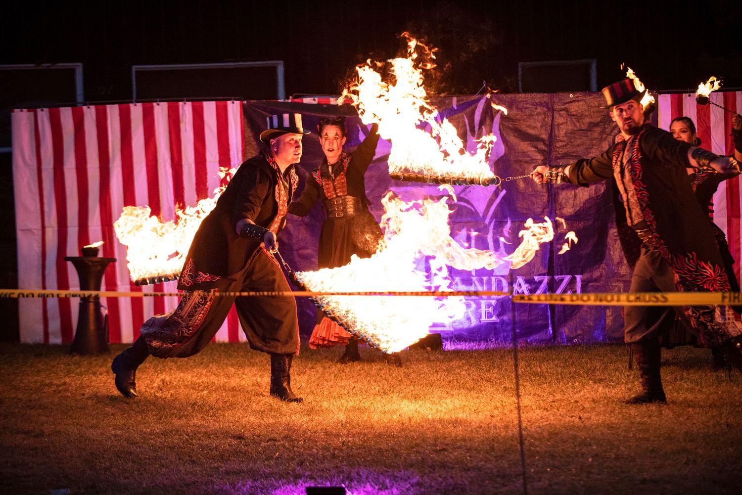 Fire performers in steampunk costumes dance with flames at a nighttime circus-themed outdoor event.Outside Monster 
Bash Harmony MN.