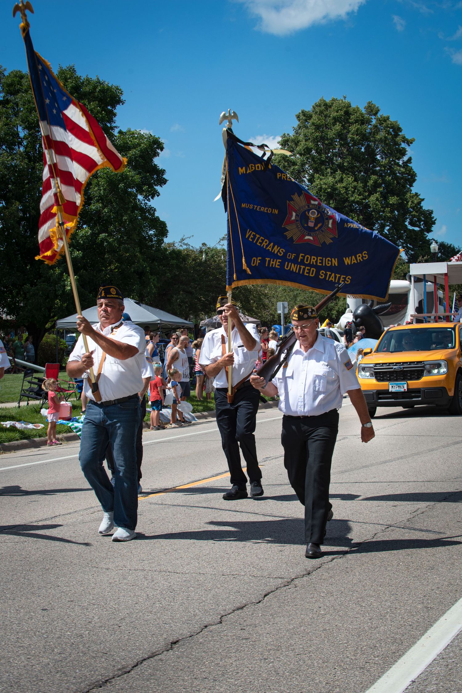 Veterans of Foreign Wars members march in a parade carrying the American flag and VFW banner on a sunny day. At Harmony MN 4th of July.