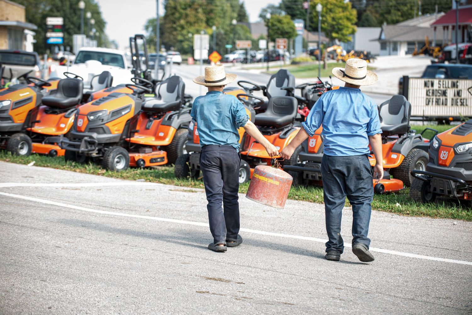 Two men in straw hats walking past a row of orange zero-turn lawn mowers at an outdoor sale.