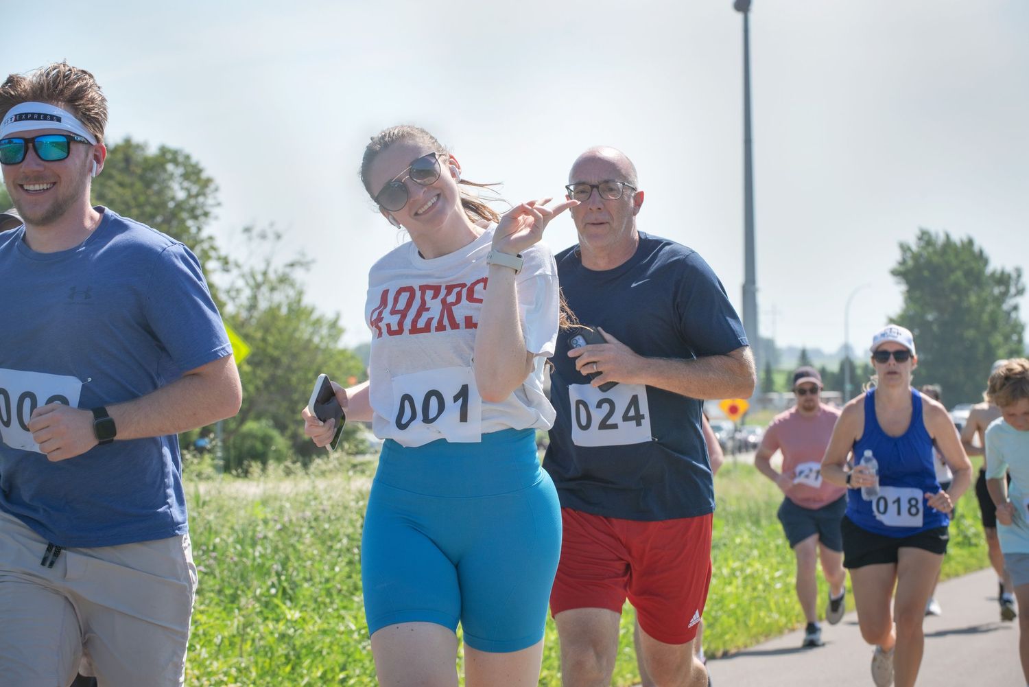 Smiling female runner wearing bib number 001 competing in outdoor road race on sunny day at Harmony MN 4th of July Celebration..