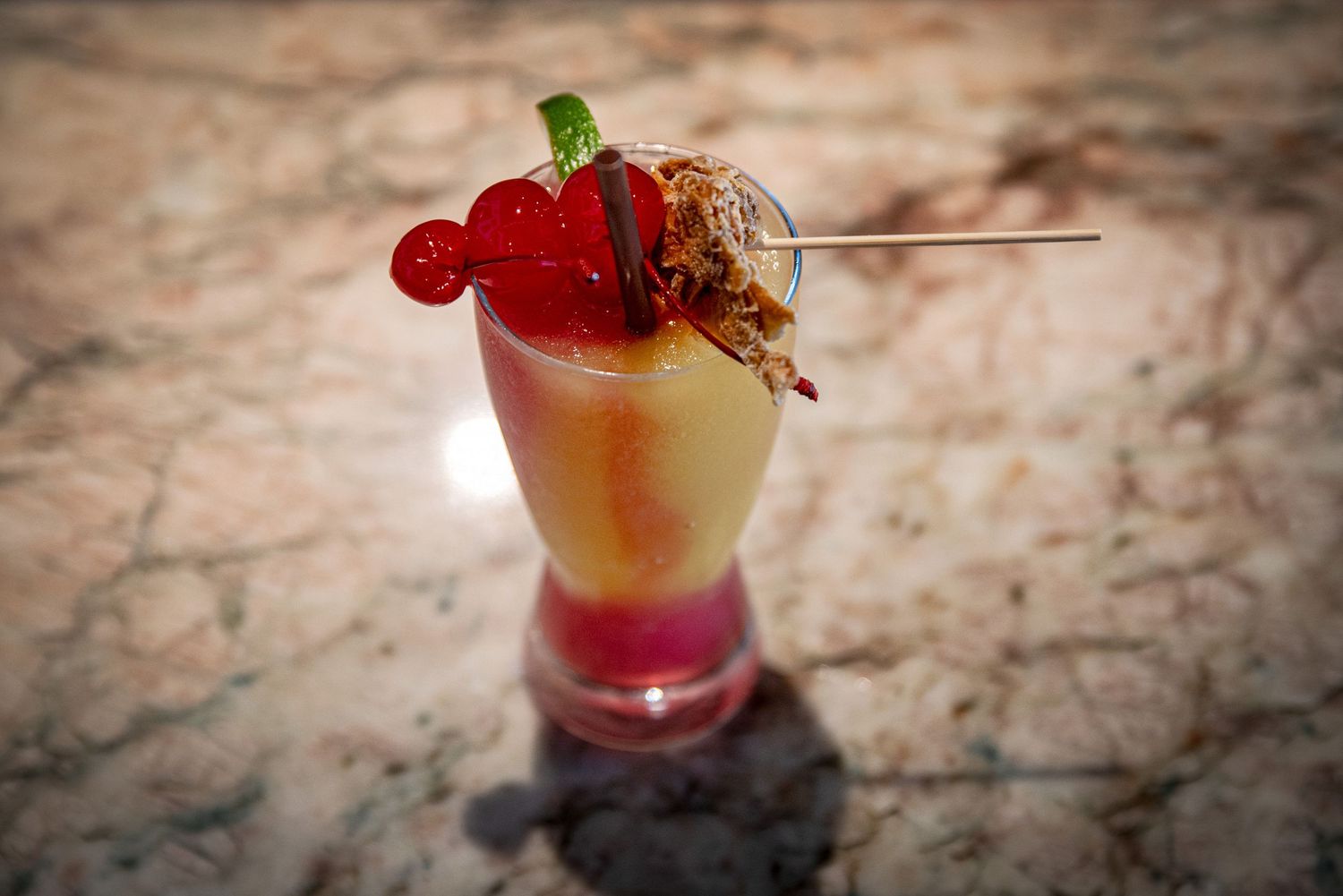 Colorful layered cocktail garnished with cherries and candied bacon in a tall glass at Estelle's Eatery.