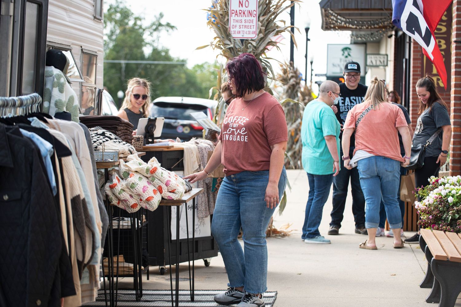 Shoppers browsing outdoor clothing displays along a small-town sidewalk storefront in front of Farm Charm.