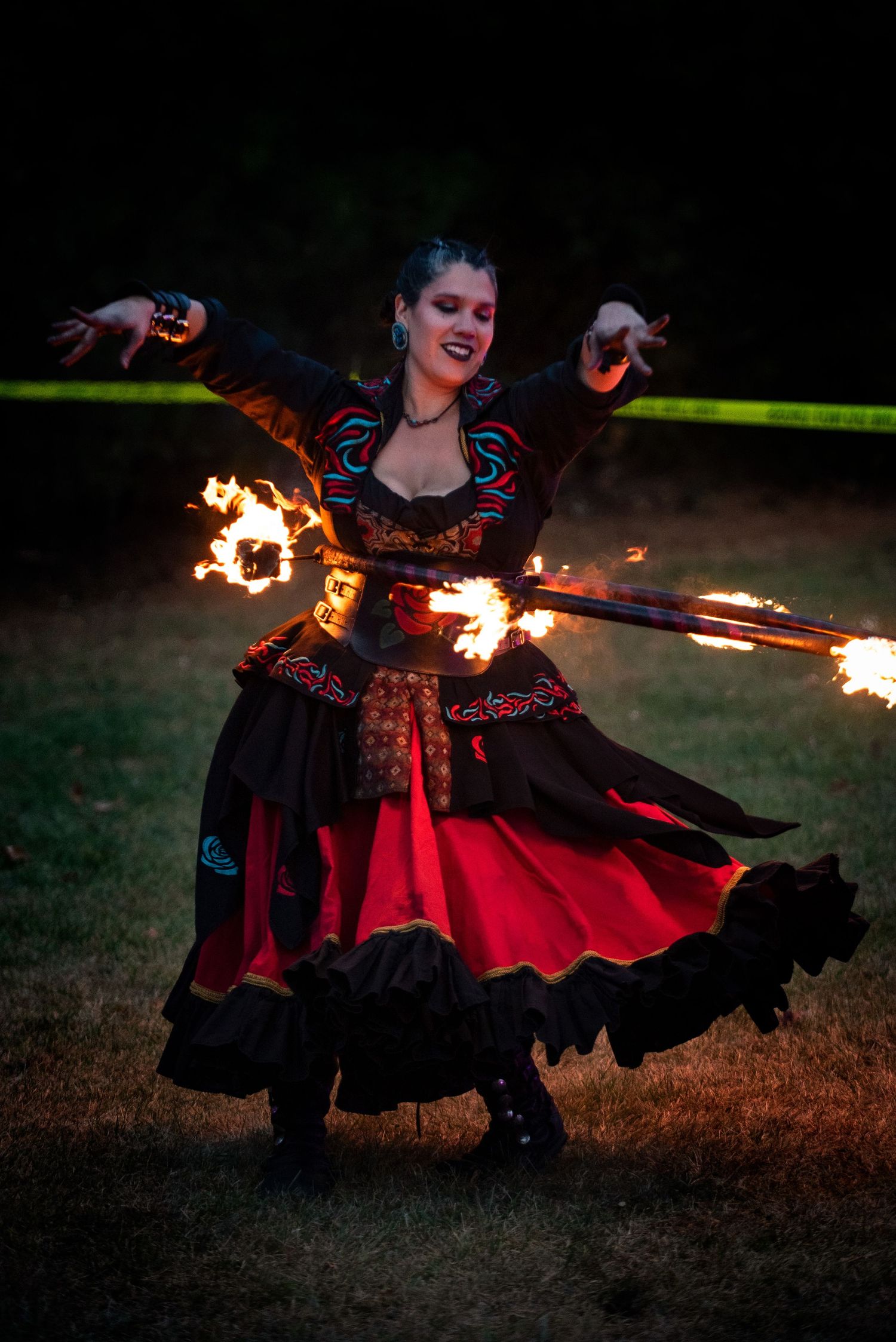 A smiling fire dancer in a red and black costume twirls flaming props during a nighttime show. Outside Monster 
Bash Harmony MN.