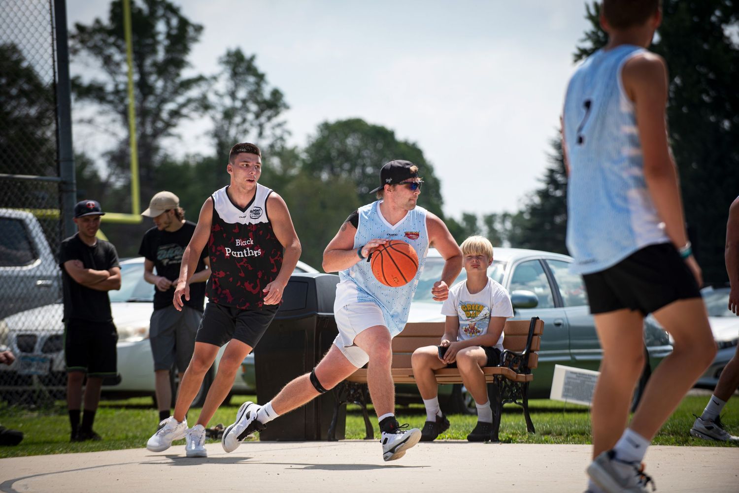 A basketball player dribbles past defenders during an outdoor Rucker League tournament game on a sunny day.