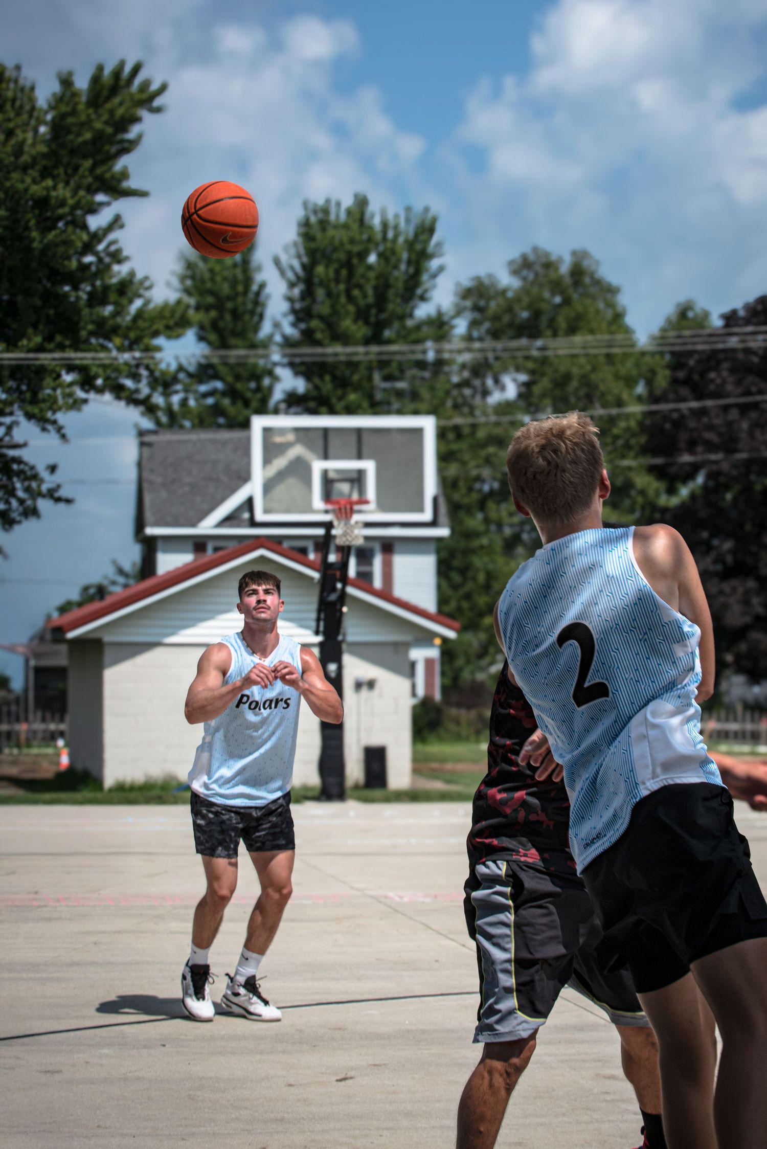 Two young men playing outdoor Rucker League basketball on a paved court on a sunny day.