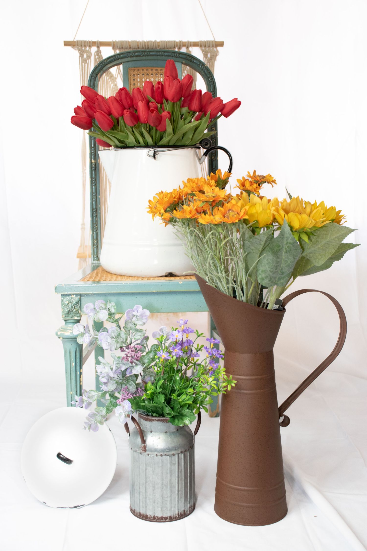 Colorful floral arrangement featuring red tulips, sunflowers, and purple wildflowers in rustic vintage pitchers and vases.