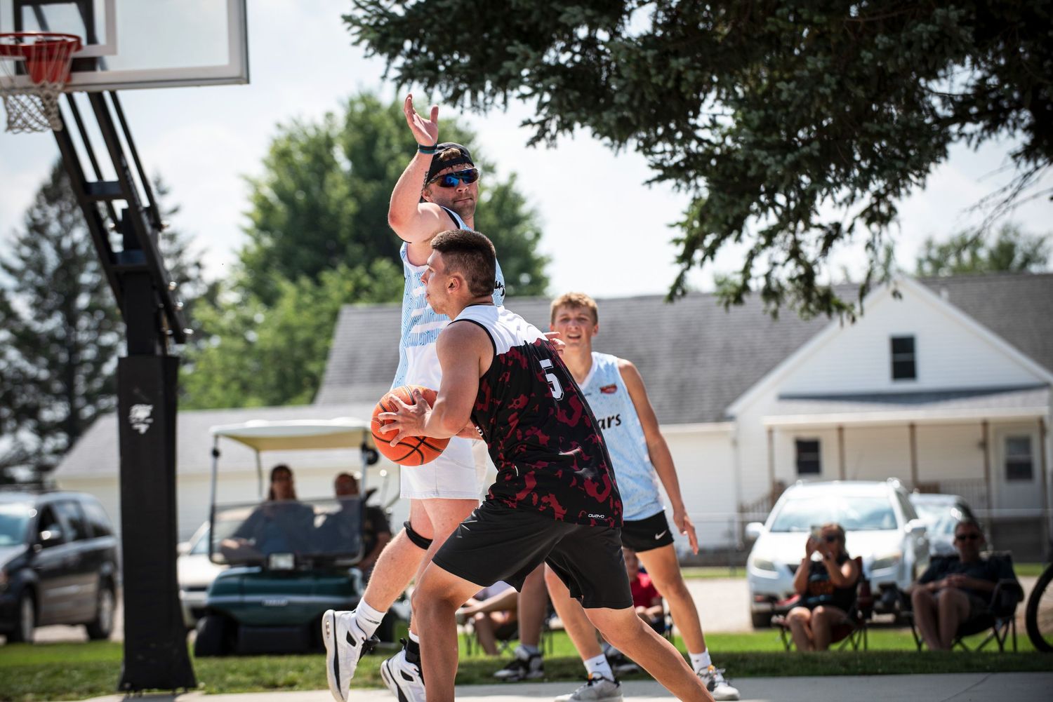 Player in blue jersey drives to basket while defender contests shot in outdoor game.