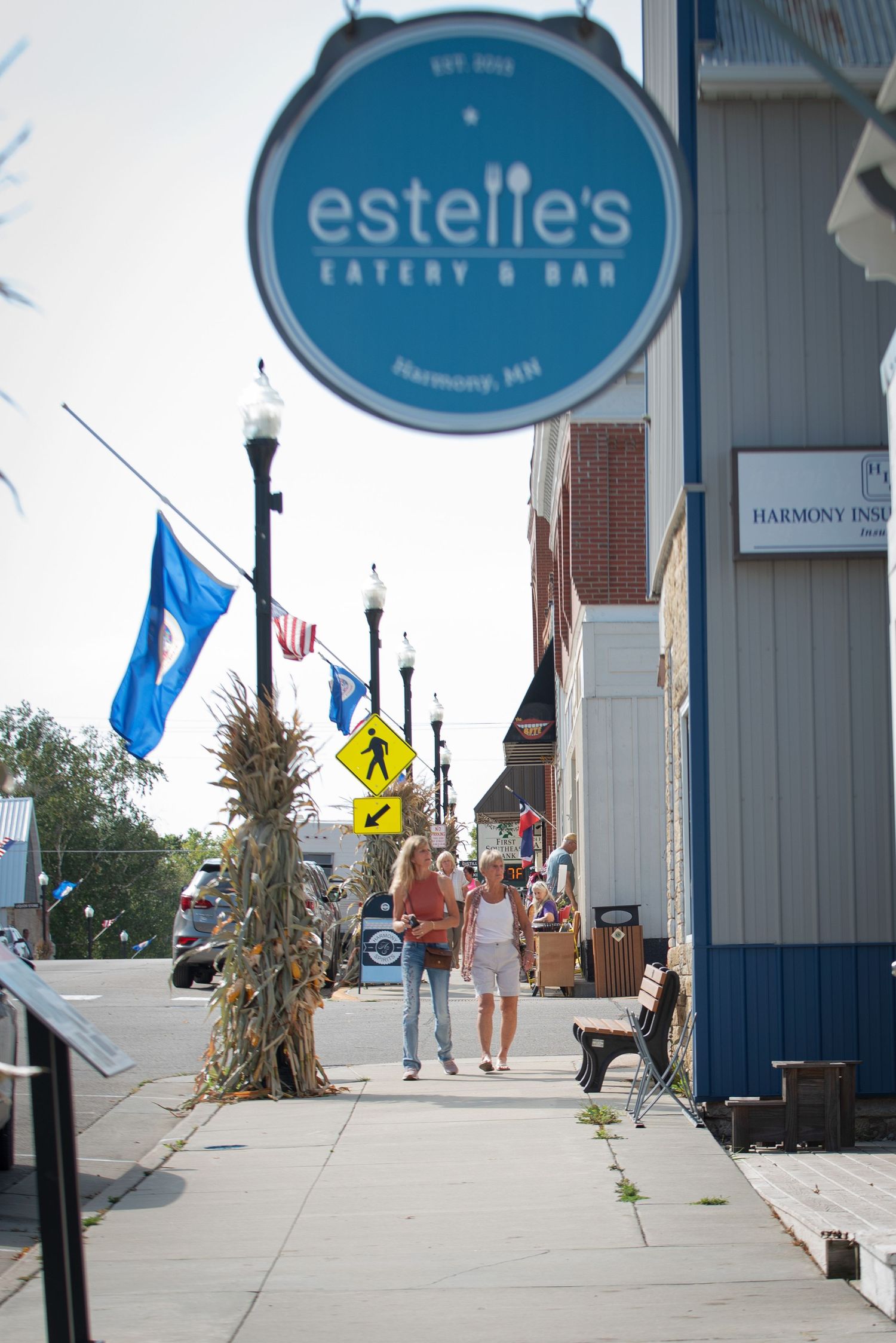 Small town main street with Estelle's Eatery and Bar sign and pedestrians on sidewalk downtown Harmony MN during the Fall to Fall Fest.
