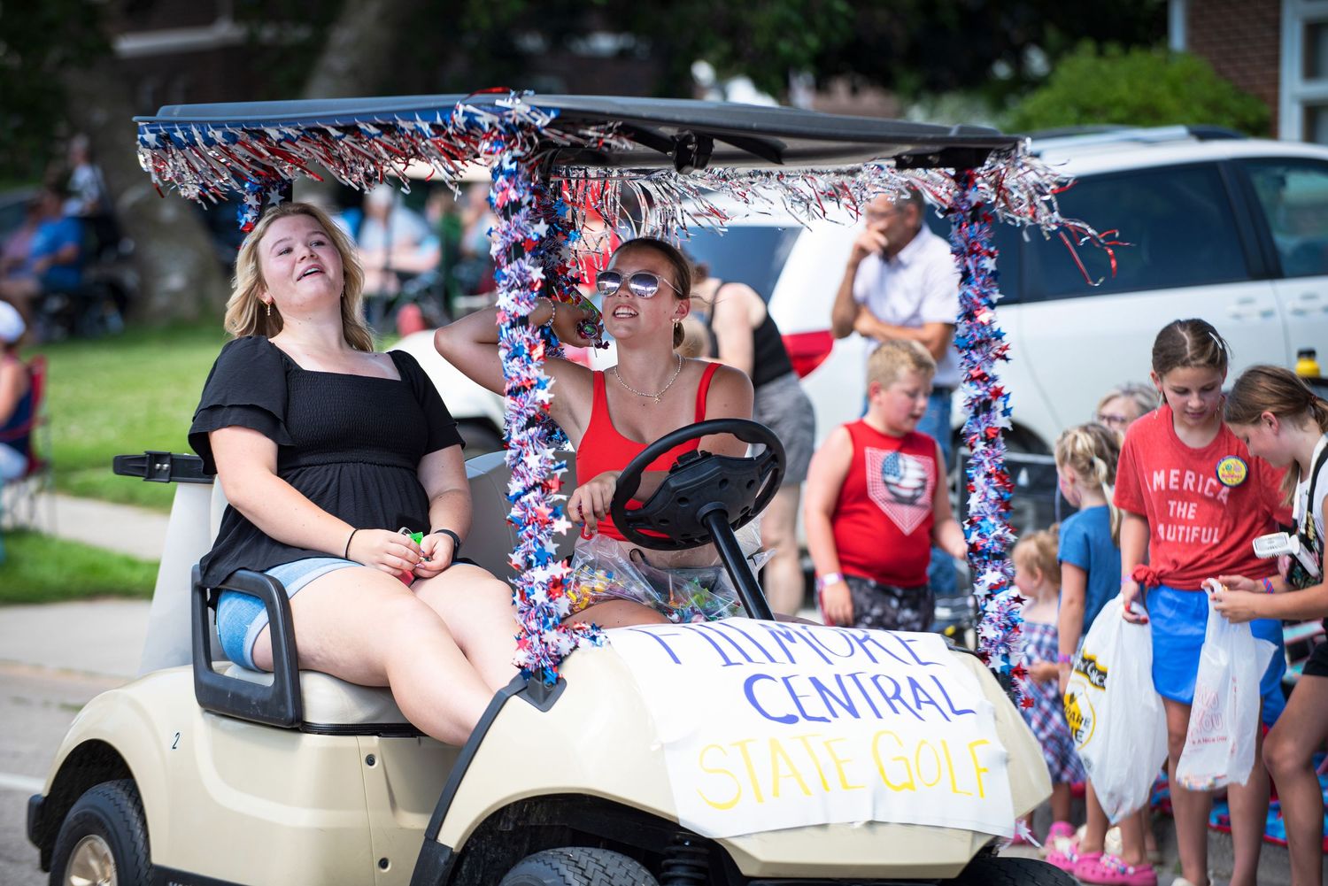 Women ride a decorated golf cart labeled Fillmore Central Staff in a festive Fourth of July parade. at Harmony MN 4th of July Celebration.