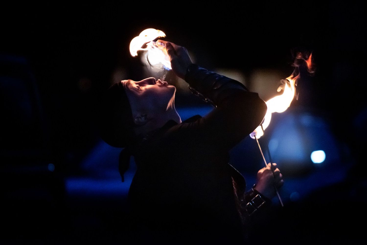A silhouetted fire eater performs with glowing flames against a dark blue night sky. Outside Monster 
Bash Harmony MN.