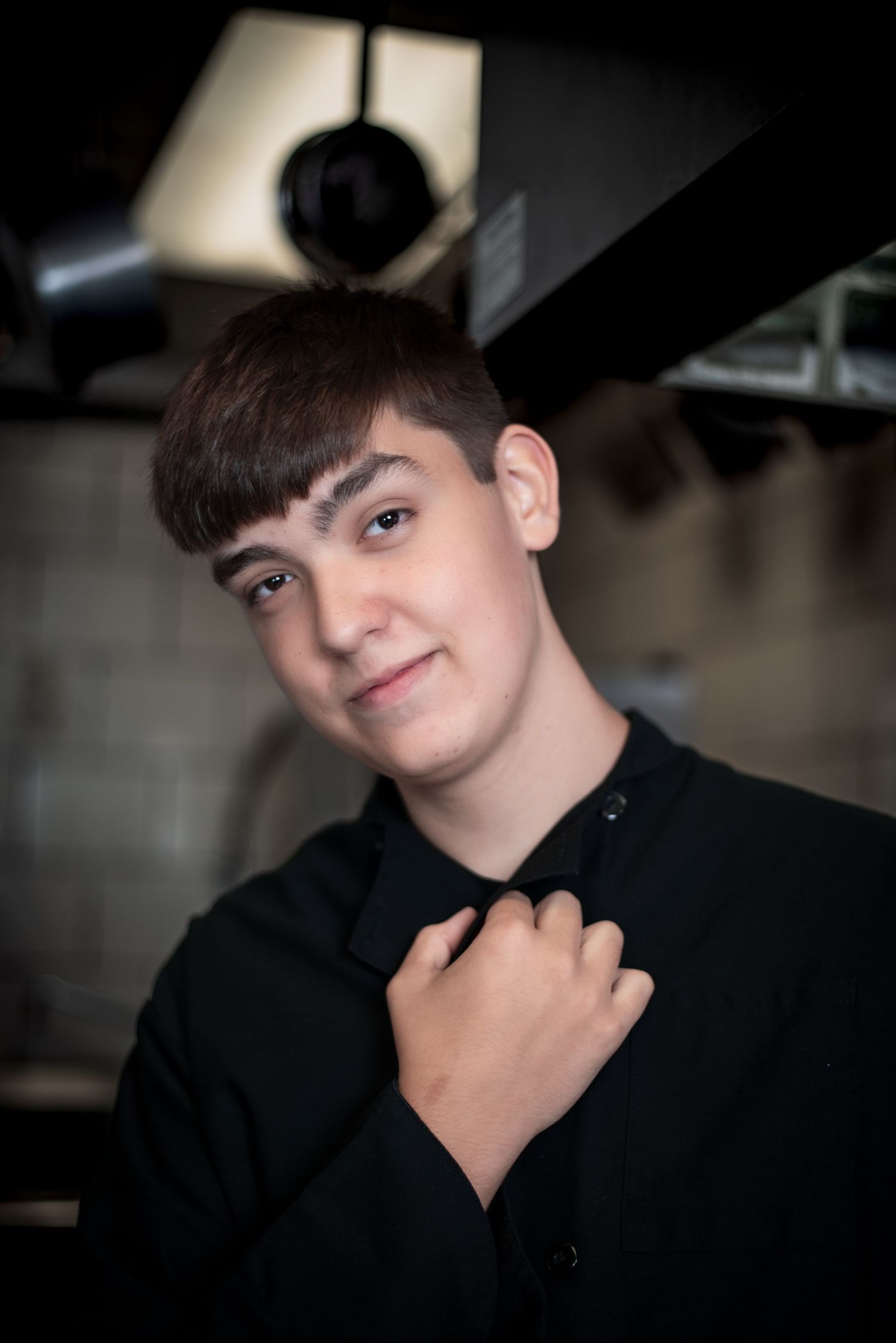 Young teen in black shirt smiling warmly in a dramatic studio portrait setting.