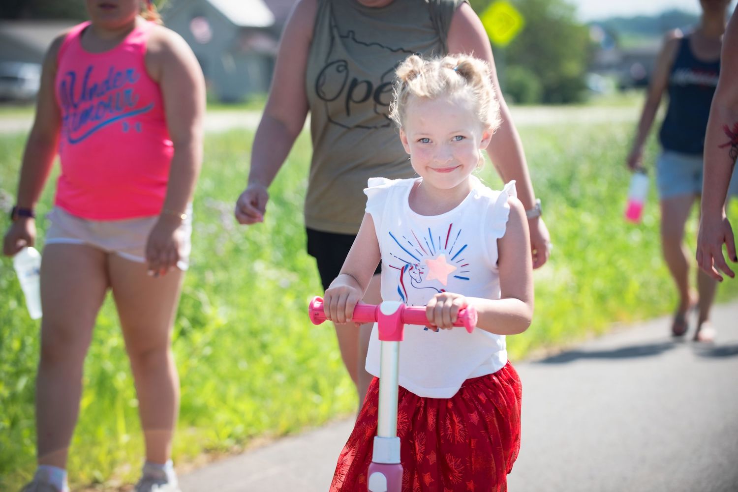 Young girl riding pink scooter in patriotic outfit on sunny summer day outdoors at Harmony MN 4th of July Celebration..