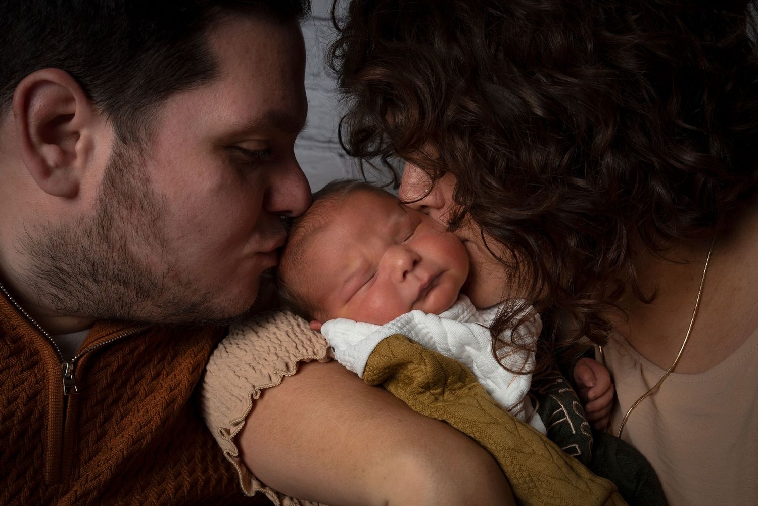 Loving parents gently kissing their sleeping newborn baby in a tender close-up portrait.