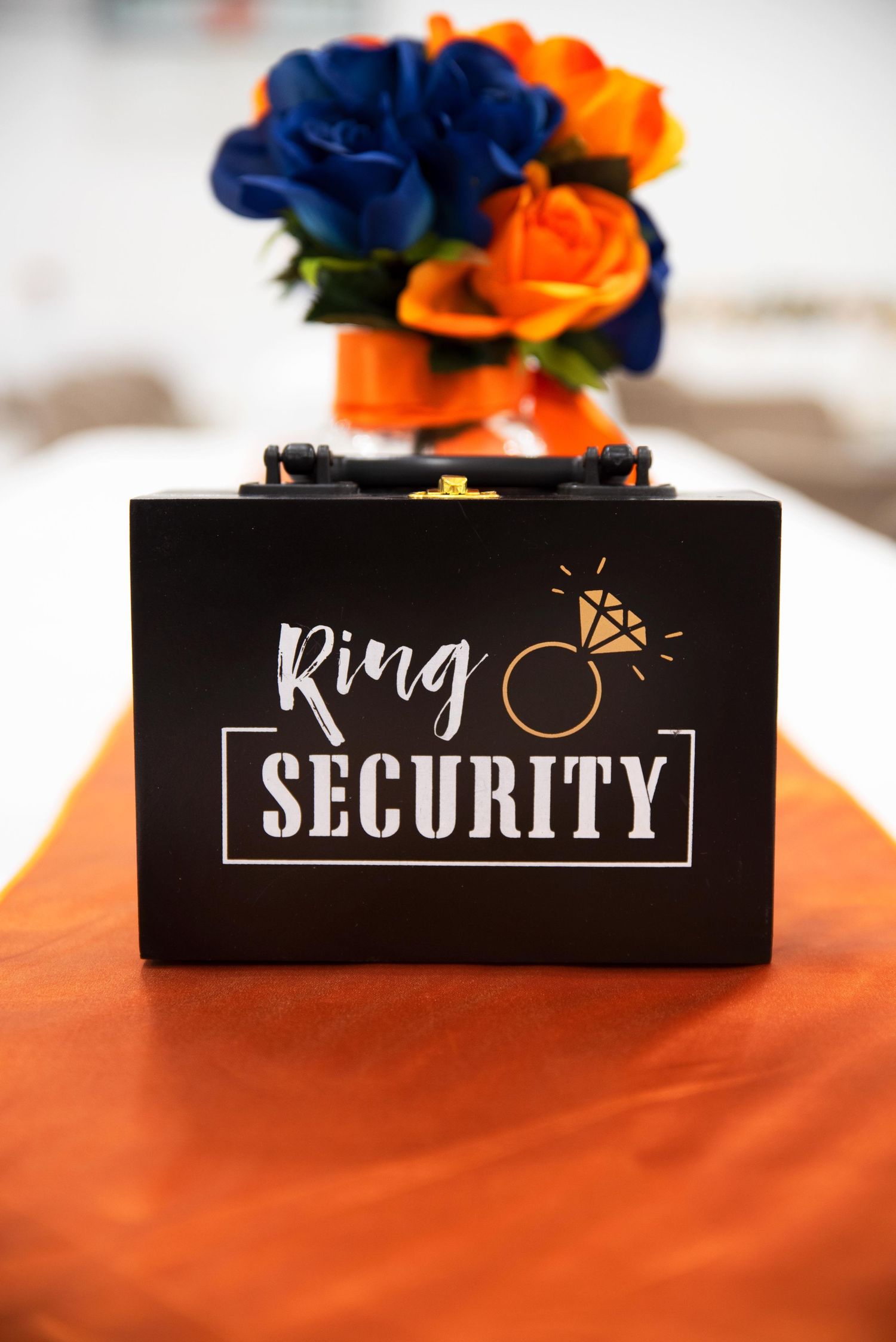 Elegant Ring Security black box with diamond ring logo on orange tablecloth at wedding reception.
