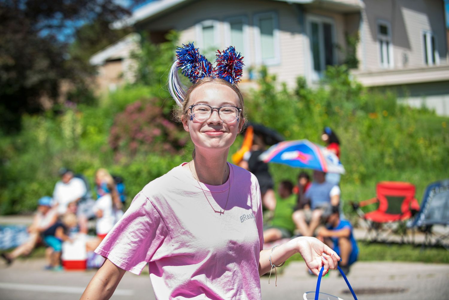 A smiling teenage girl wearing patriotic Minnie Mouse ears walks in a sunny Fourth of July parade at Harmony MN 4th of July Celebration..