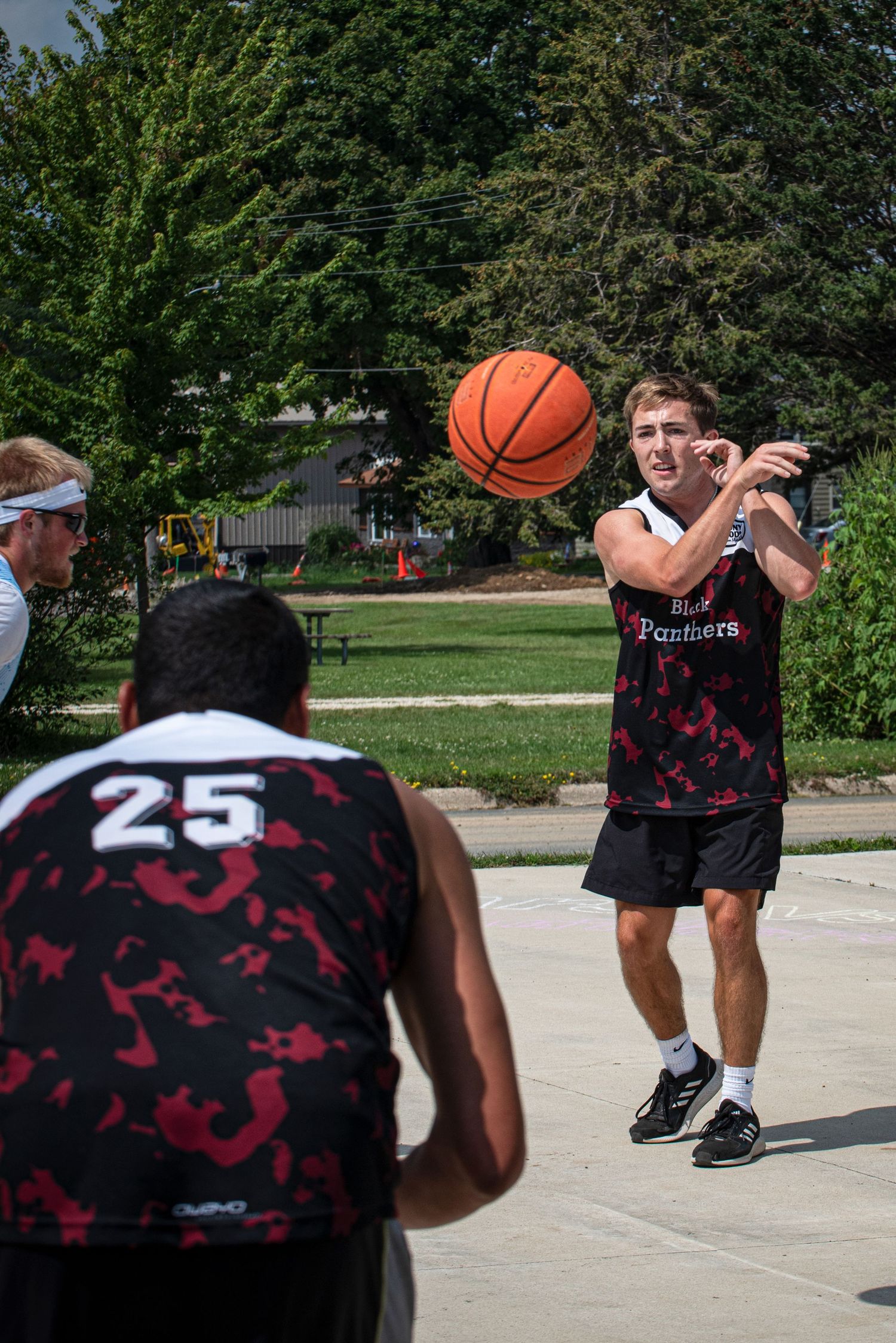 Player in black Panthers jersey passes basketball to teammate during outdoor Rucker League game.
