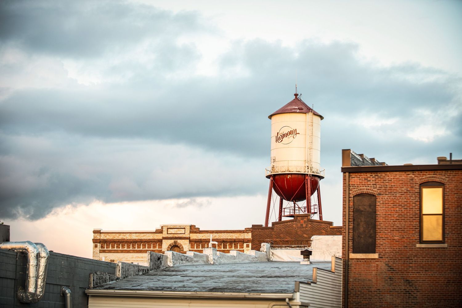 Historic Lagunitas brewery water tower rising above brick rooftops under a cloudy sunset sky.