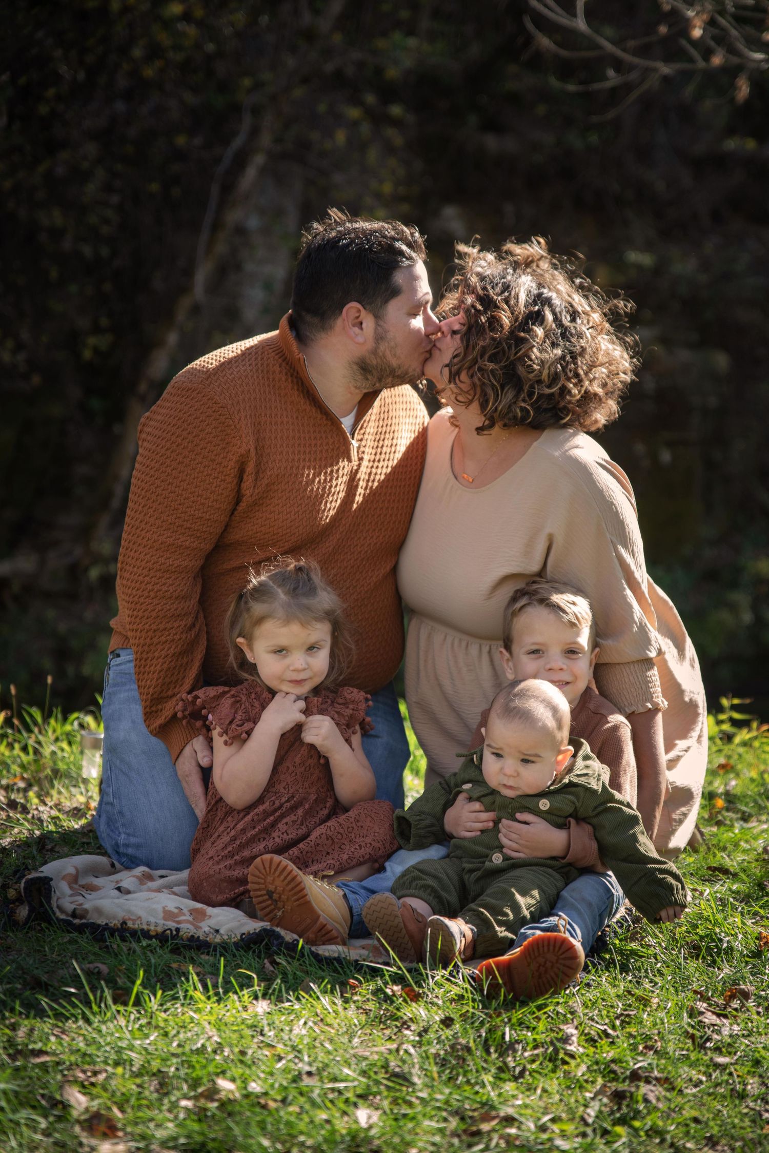 Happy family of five sharing a tender moment sitting together on sunny green grass.