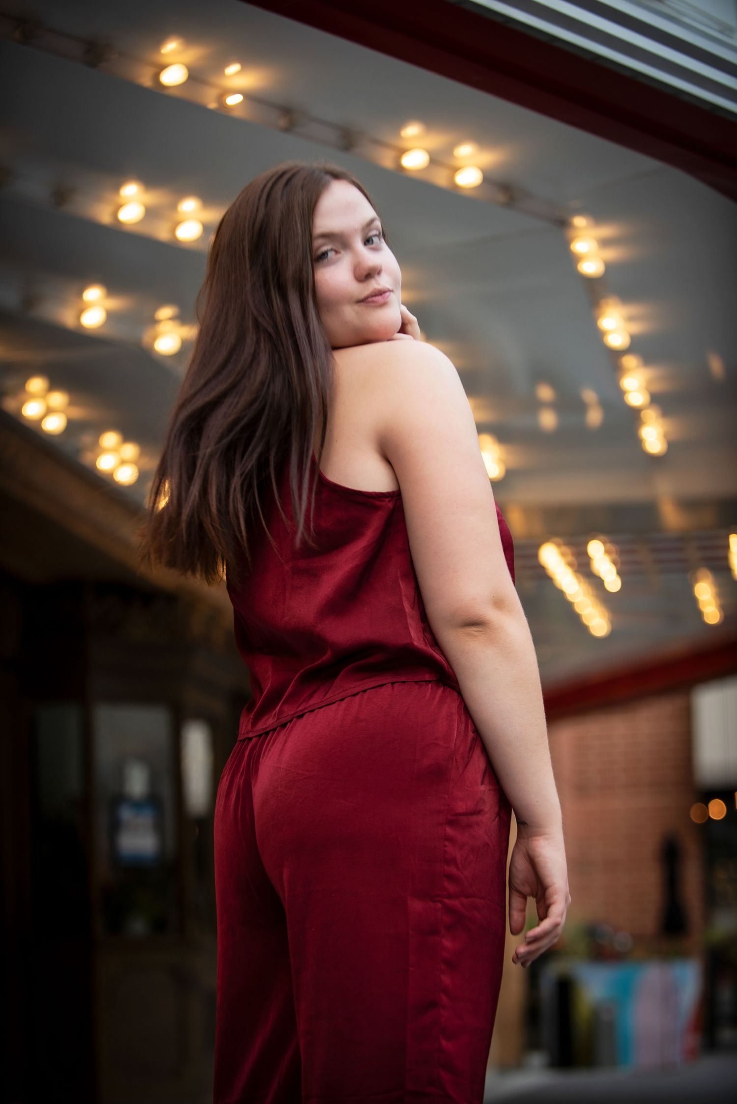 Young woman in elegant red jumpsuit posing under marquee lights at night.