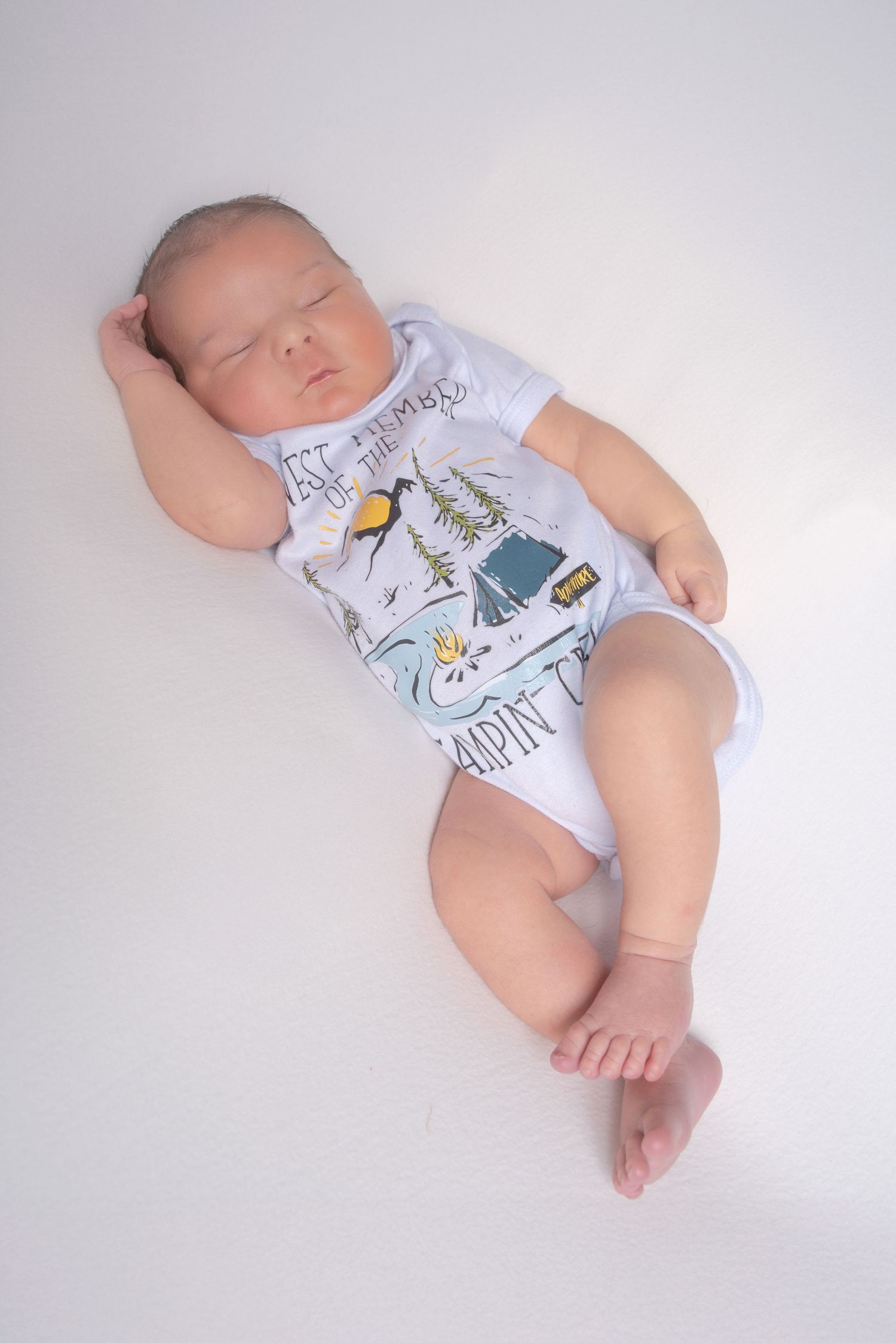 Peaceful newborn baby sleeping in a camping-themed onesie on white background.