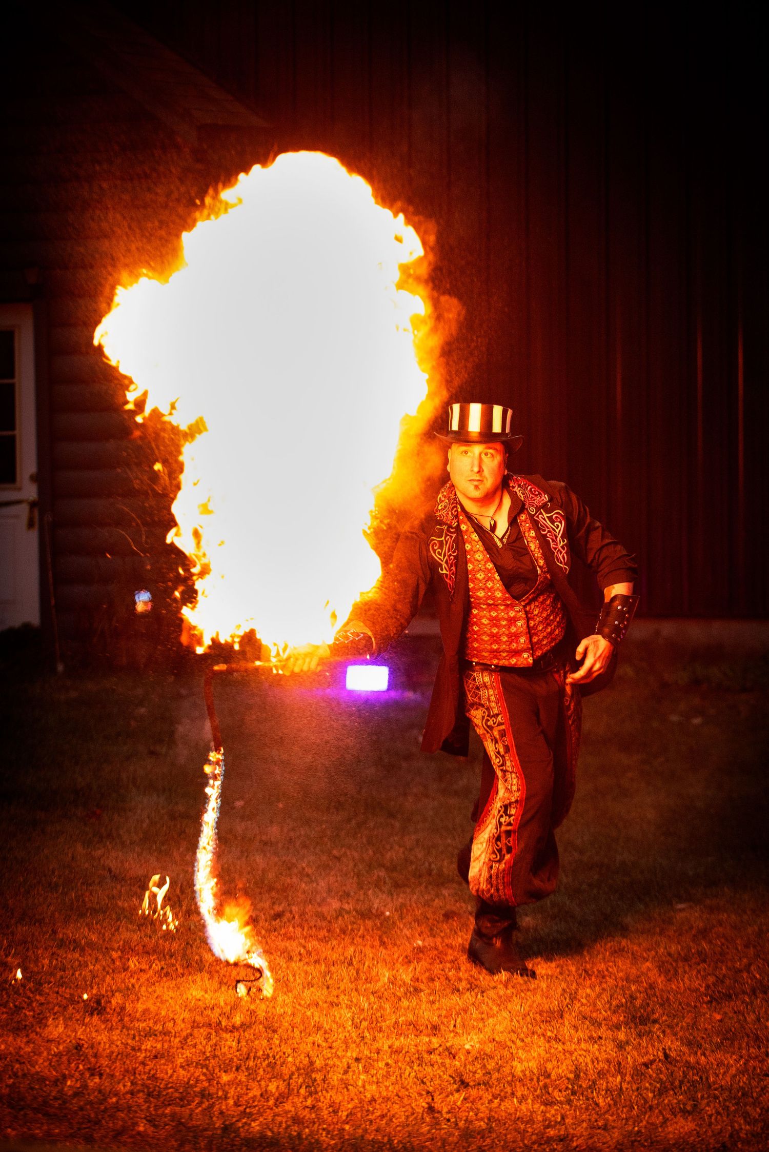 A fire breather in a striped top hat creates a massive fireball during an outdoor night show.Outside Monster 
Bash Harmony MN.