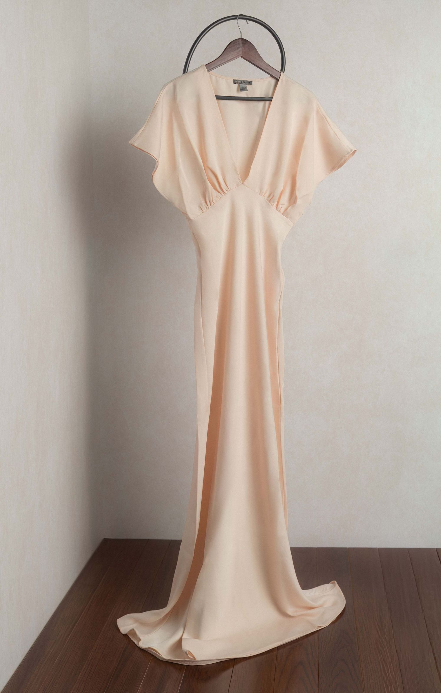 Elegant blush pink maxi dress with flutter sleeves and deep V-neckline, displayed on a hanger against a neutral wall.
