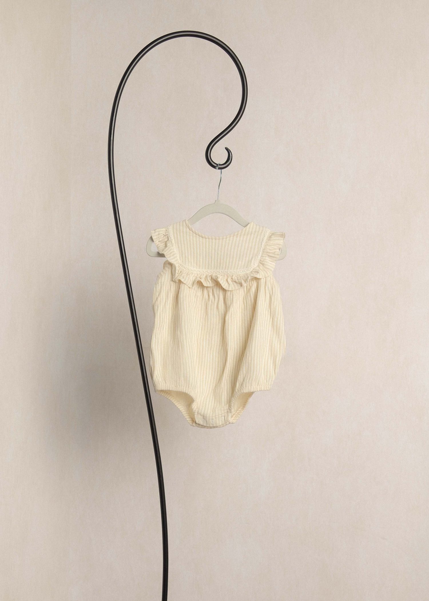 Cream striped ruffle baby romper hanging on a decorative hook against a neutral background.