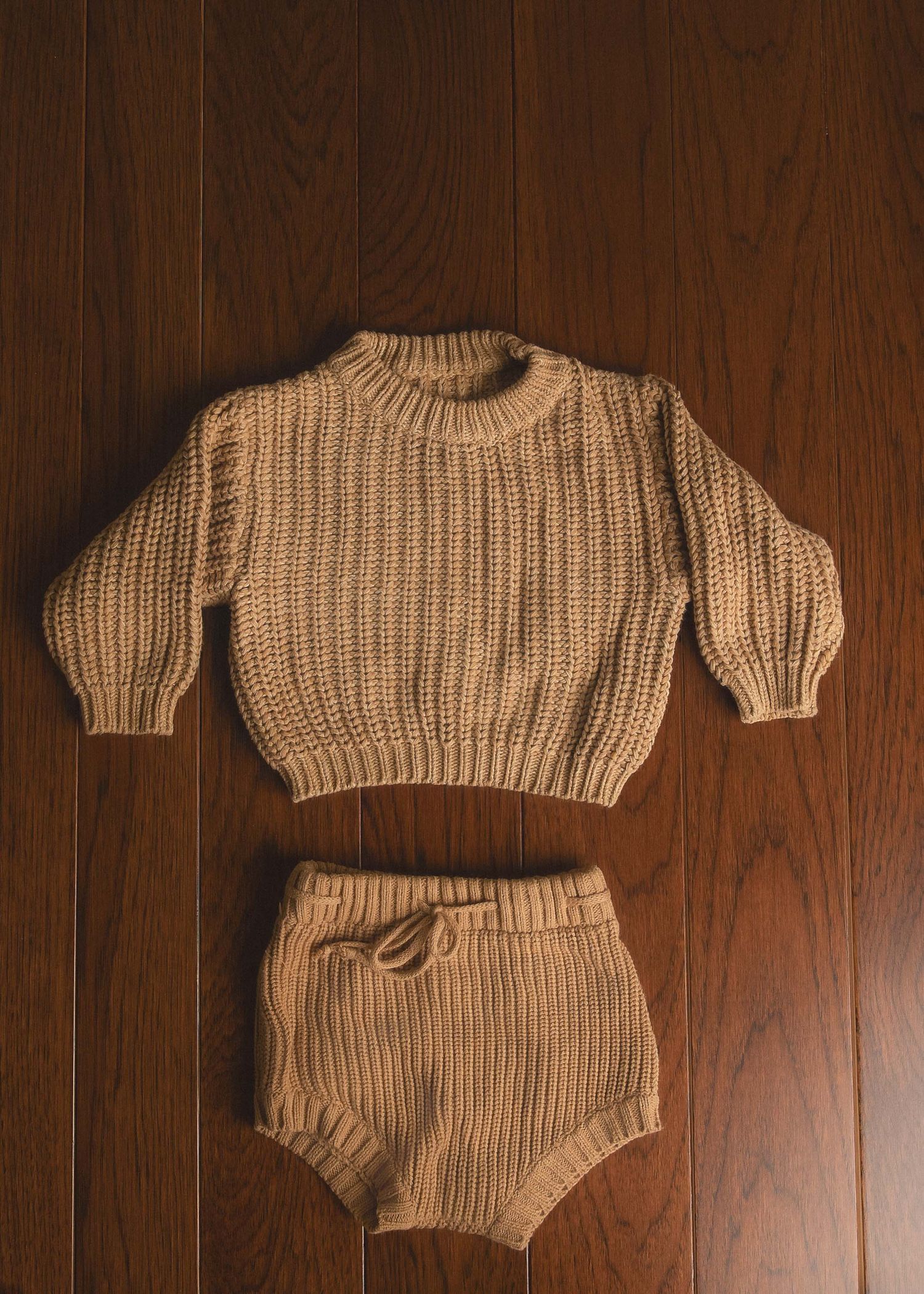 Camel chunky knit baby sweater and matching bloomers set laid flat on wood surface.