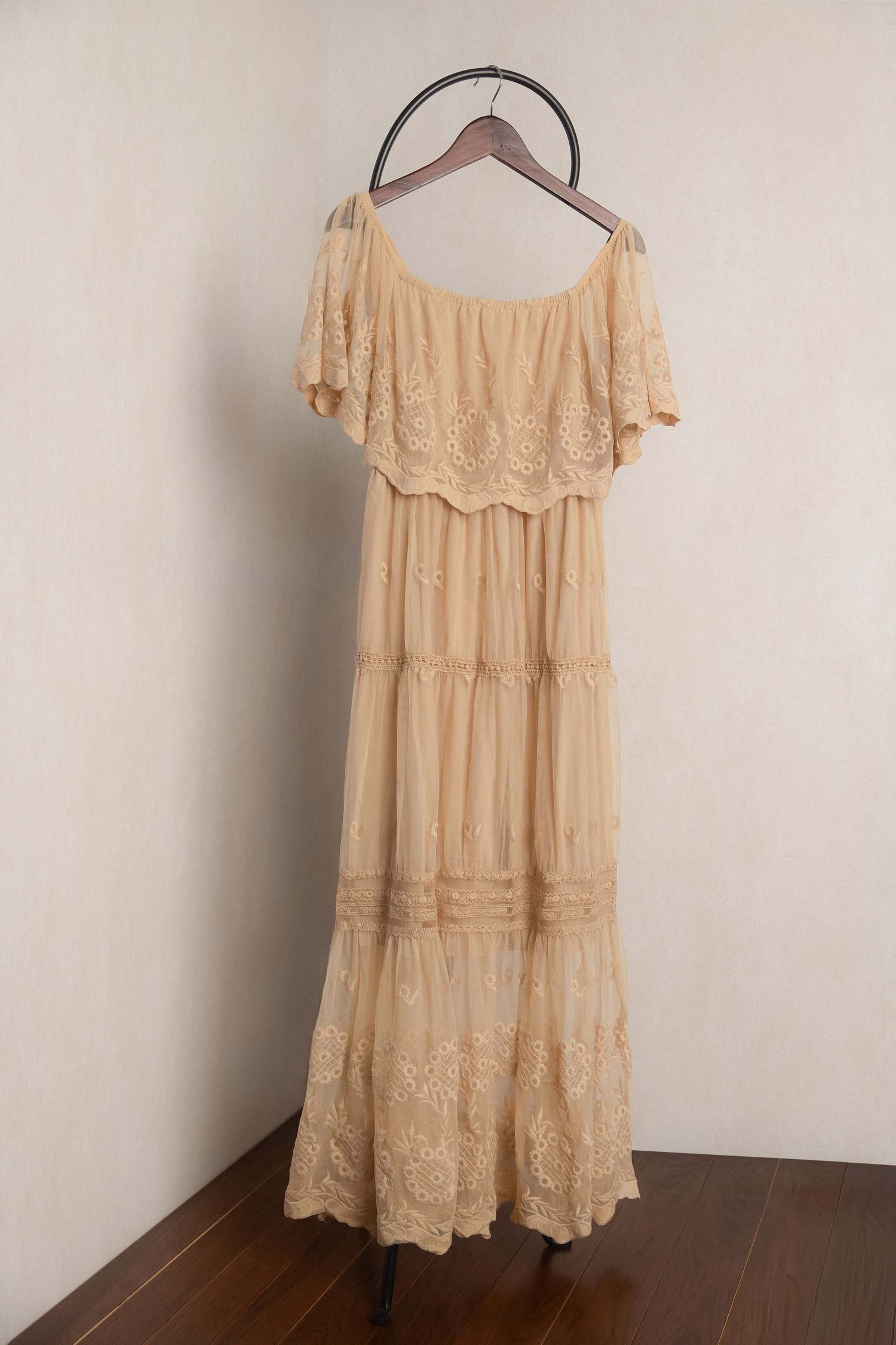 Elegant cream lace maxi dress with off-shoulder ruffle neckline and tiered skirt, displayed on a hanger.