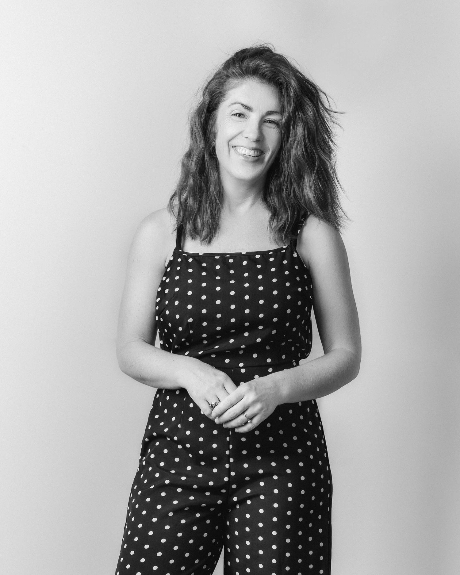 Black and white photo of a smiling woman in a polka dot jumpsuit posing against a light background.