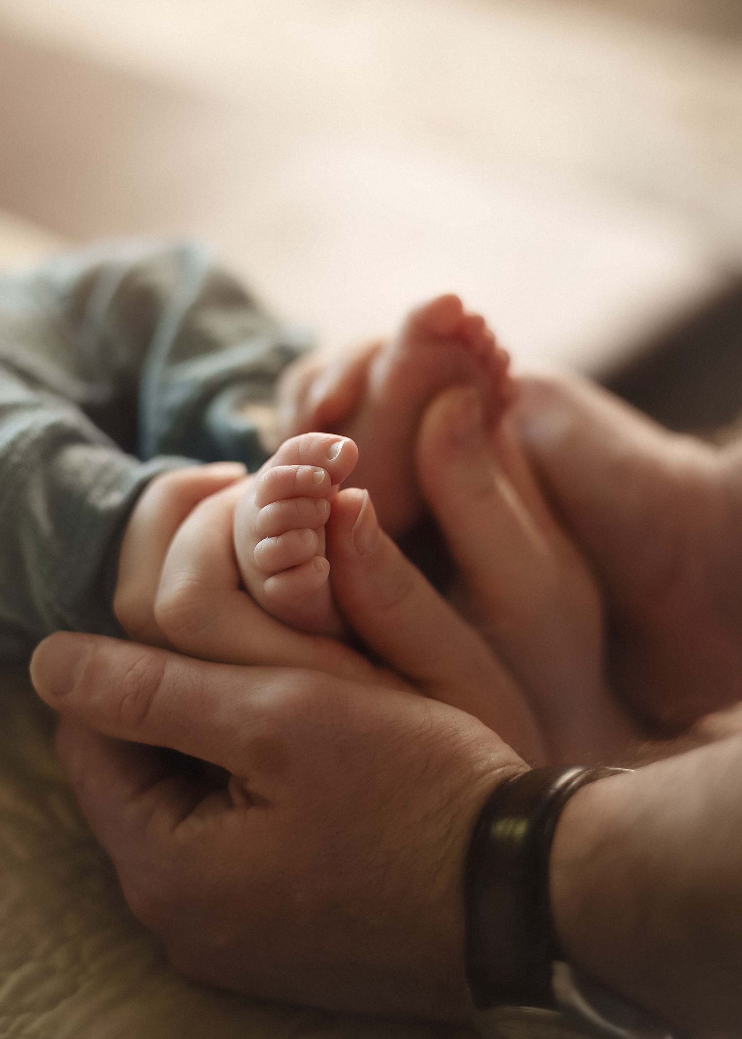 Adult hands gently cradling tiny newborn baby feet, capturing a tender moment of parental love and new life.