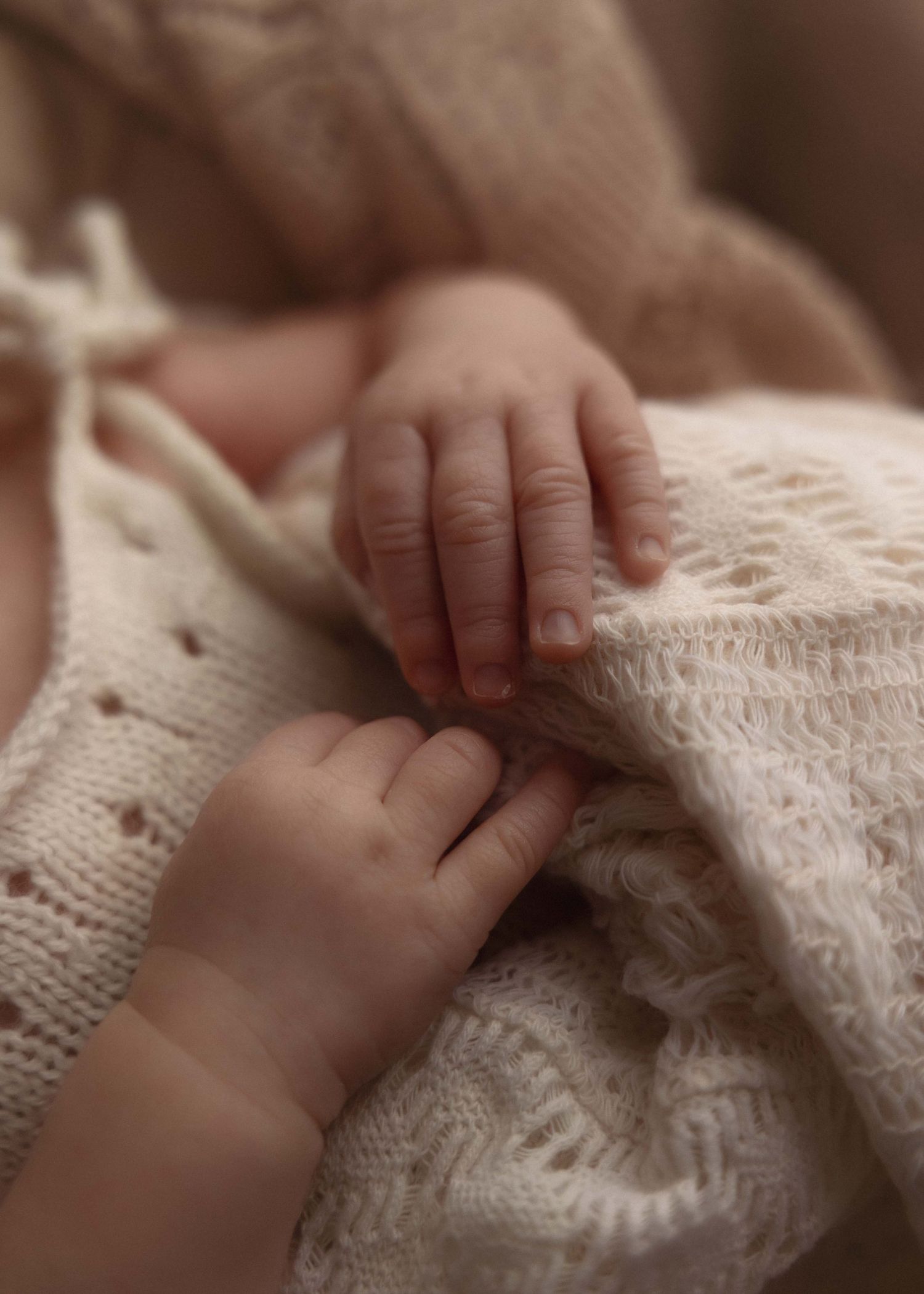Close-up of tiny newborn baby hands resting on a soft cream knitted blanket, capturing delicate infant details.