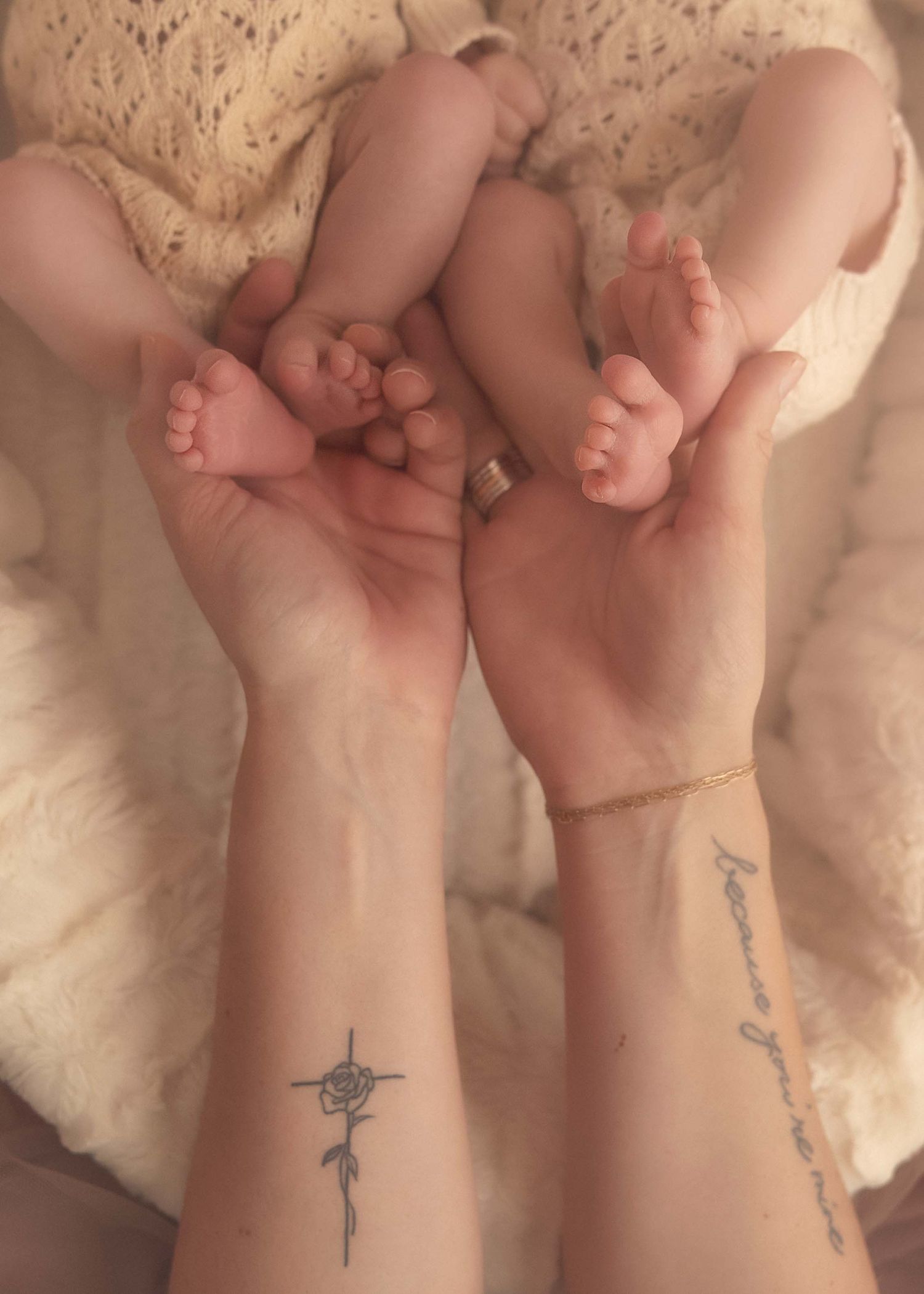 Parents holding newborn twins tiny feet together showing wrist tattoos in newborn photography.