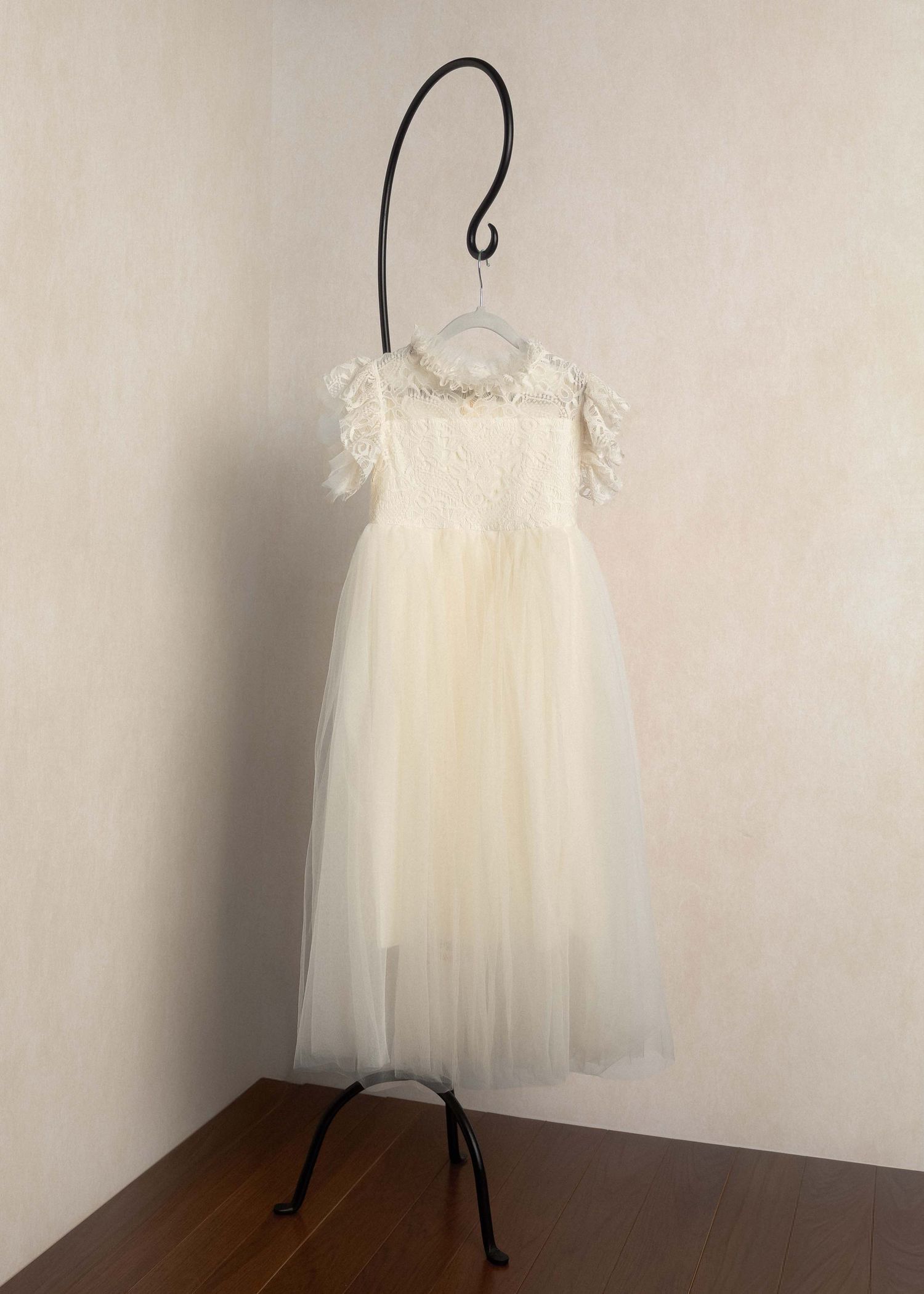 Ivory flower girl dress with lace bodice, feather sleeves, pearl neckline, and tulle skirt on a decorative hanger.