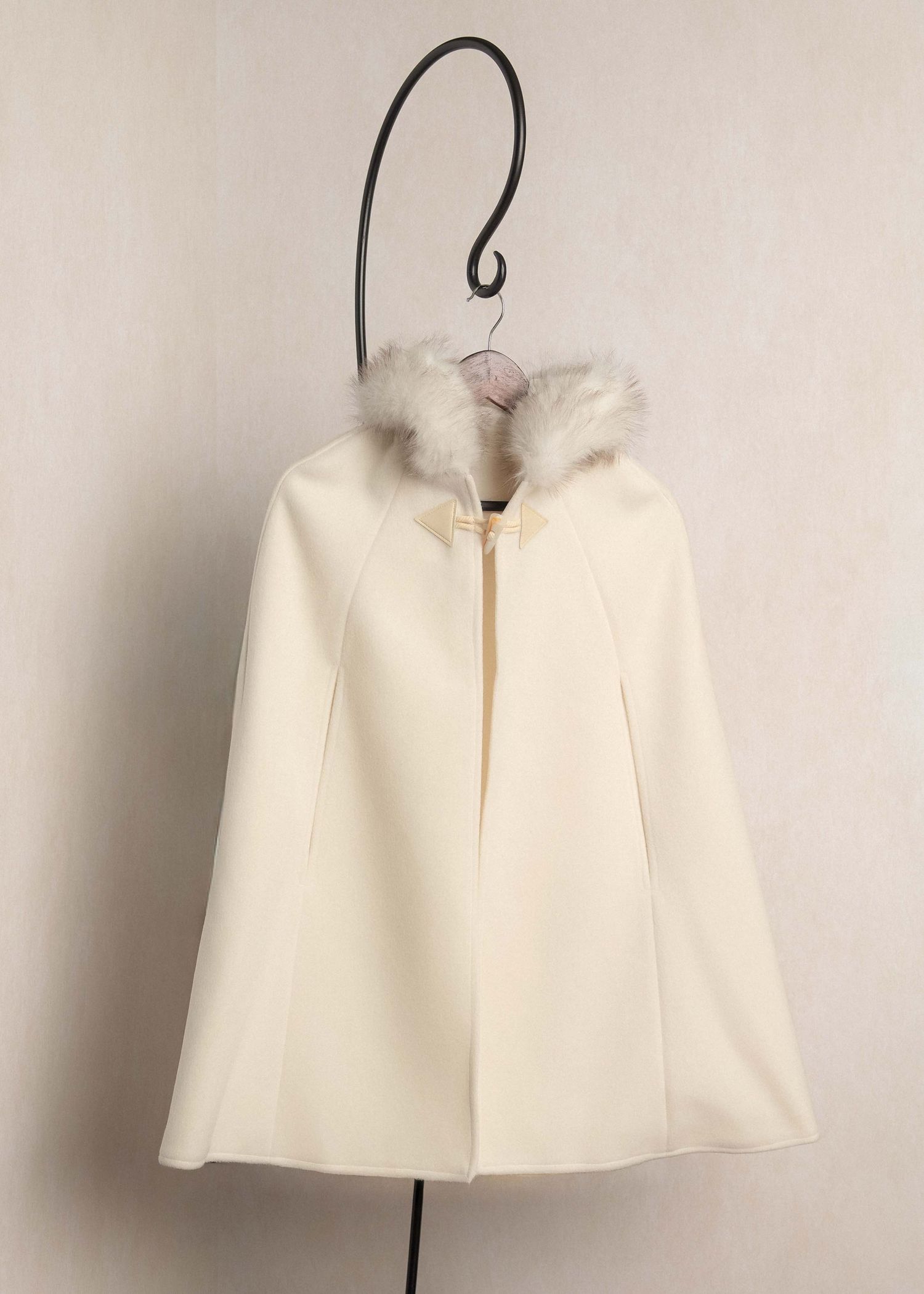 Ivory white wool cape with fluffy fur collar displayed on a decorative hook hanger against a white background.