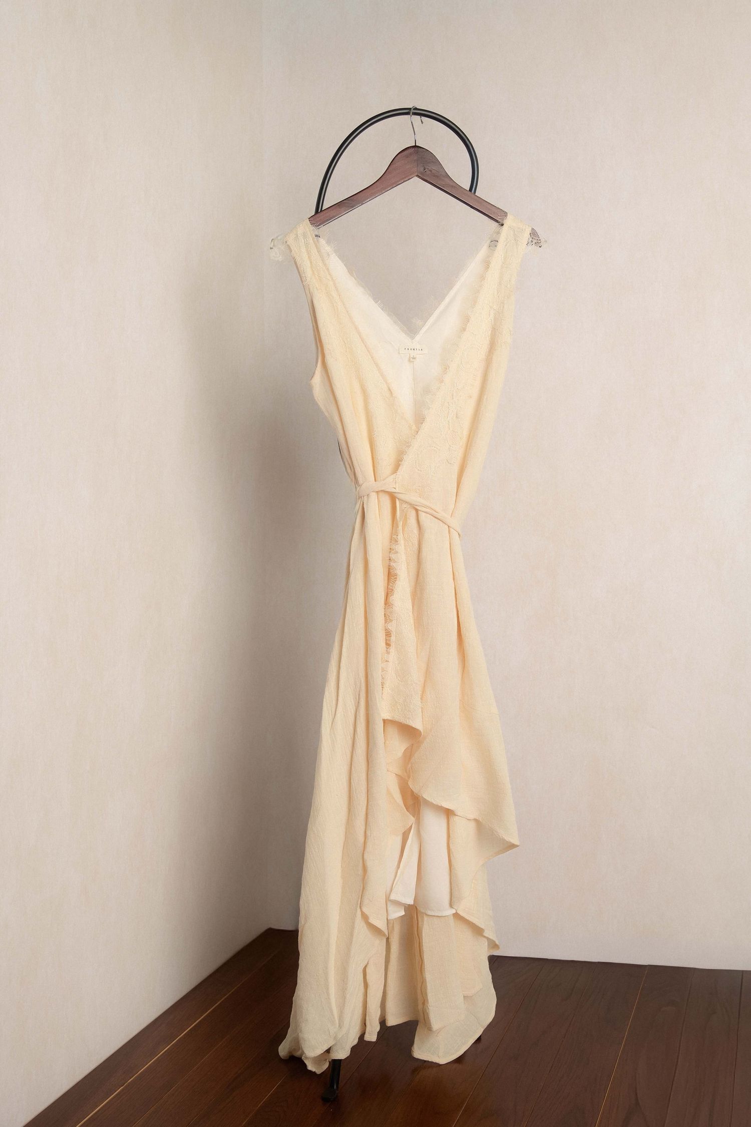 Elegant cream chiffon sleeveless wrap dress with ruffle hem on wooden hanger against neutral wall.