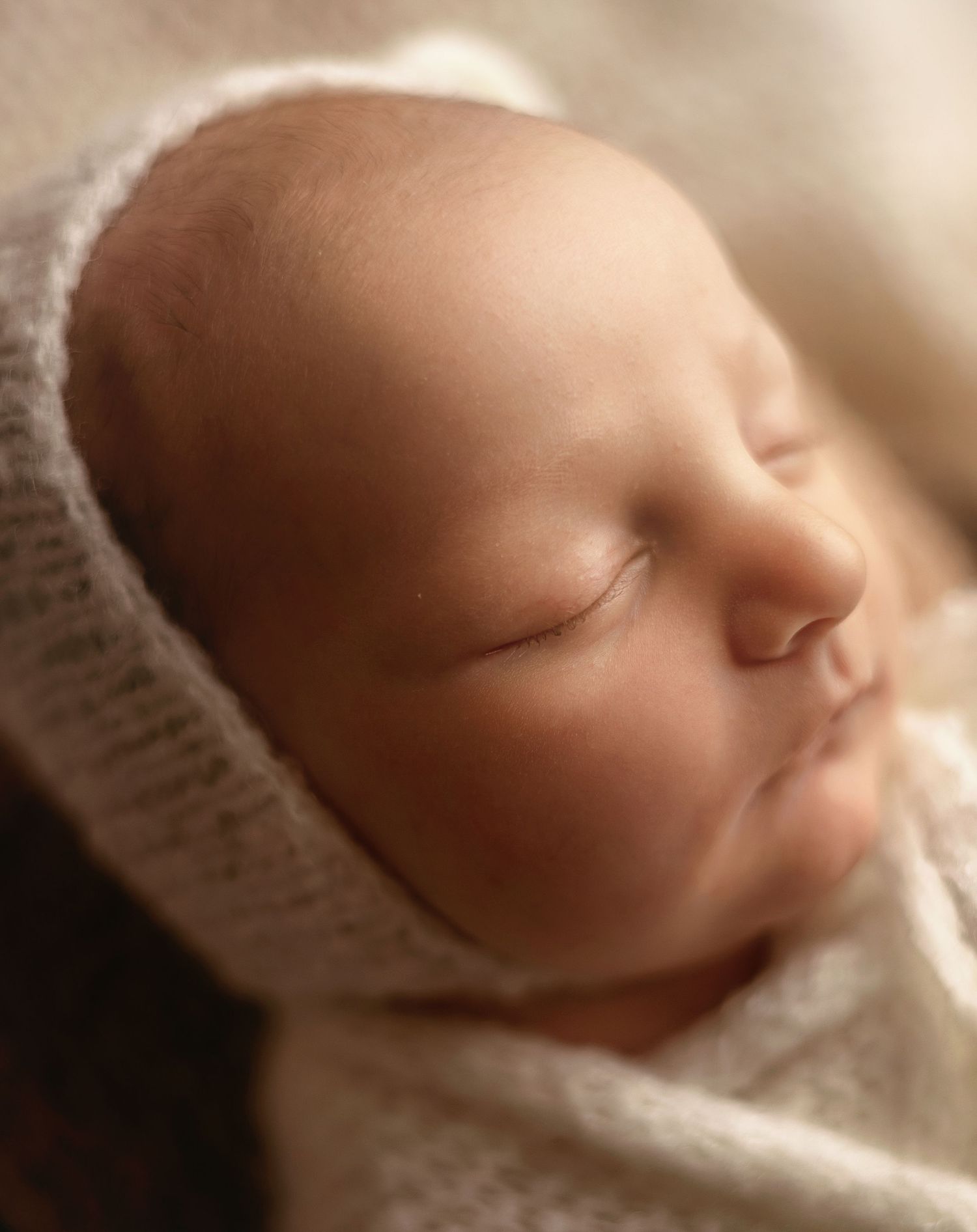 Peaceful newborn baby sleeping wrapped in a soft white knit blanket and bonnet, close-up portrait photography.