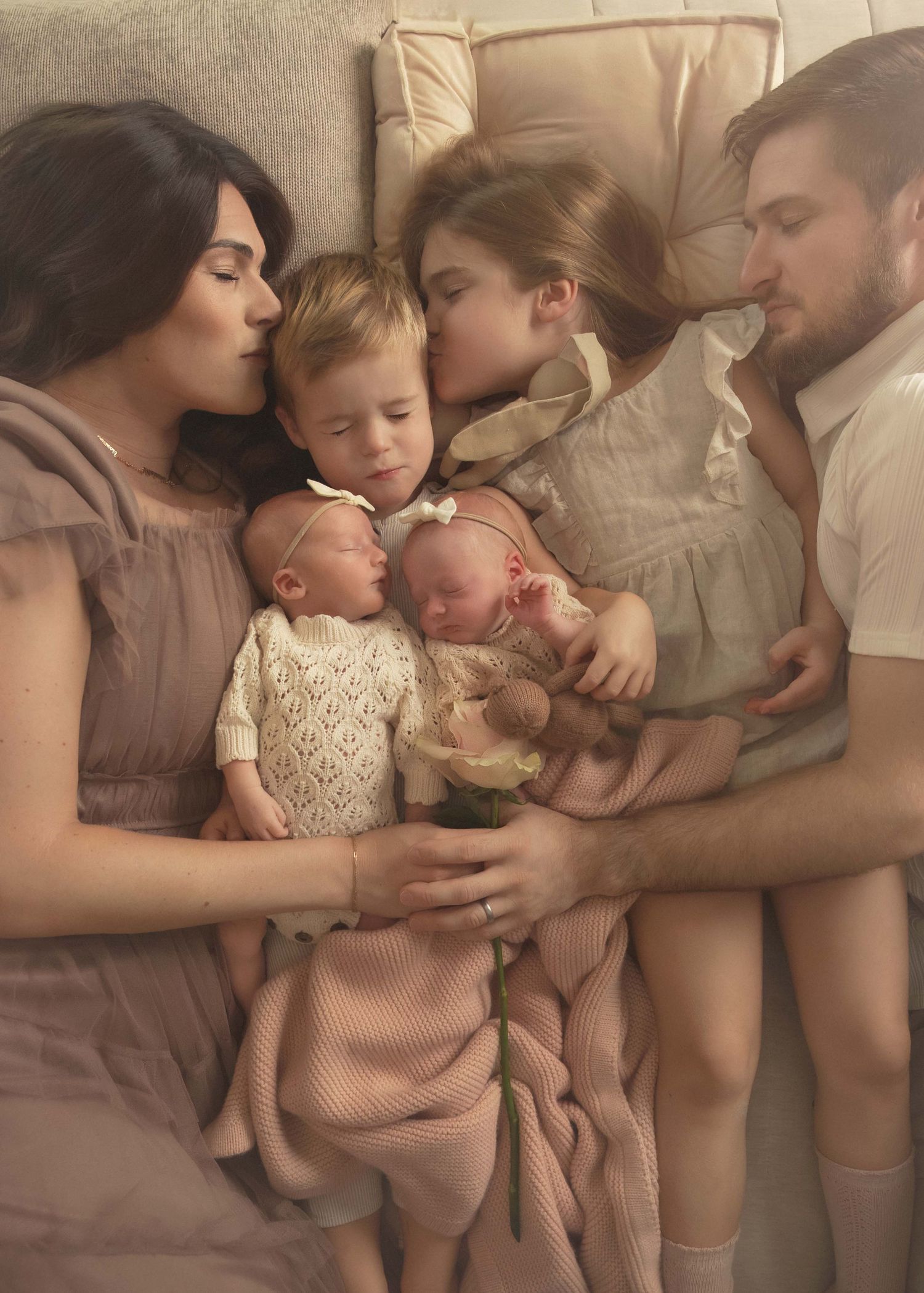 Family portrait of parents with two toddlers and newborn twins lying together on a cozy bed.