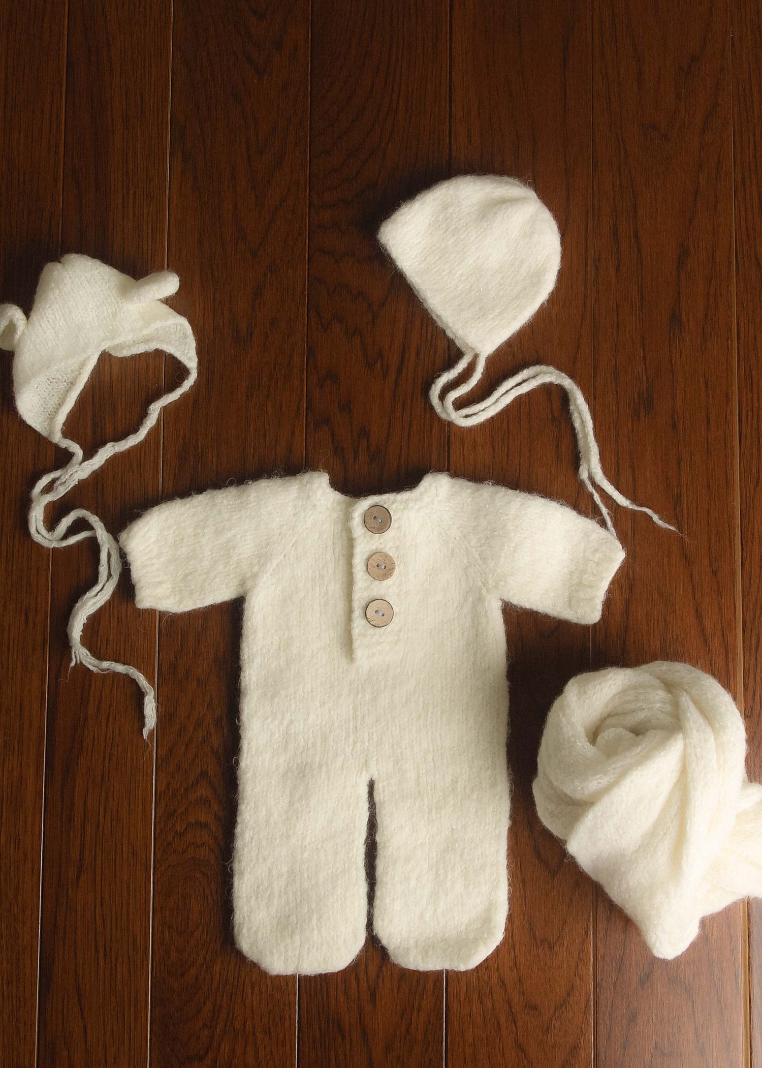 White knit newborn baby romper set with two bonnets and blanket on wooden floor, perfect for photography props.